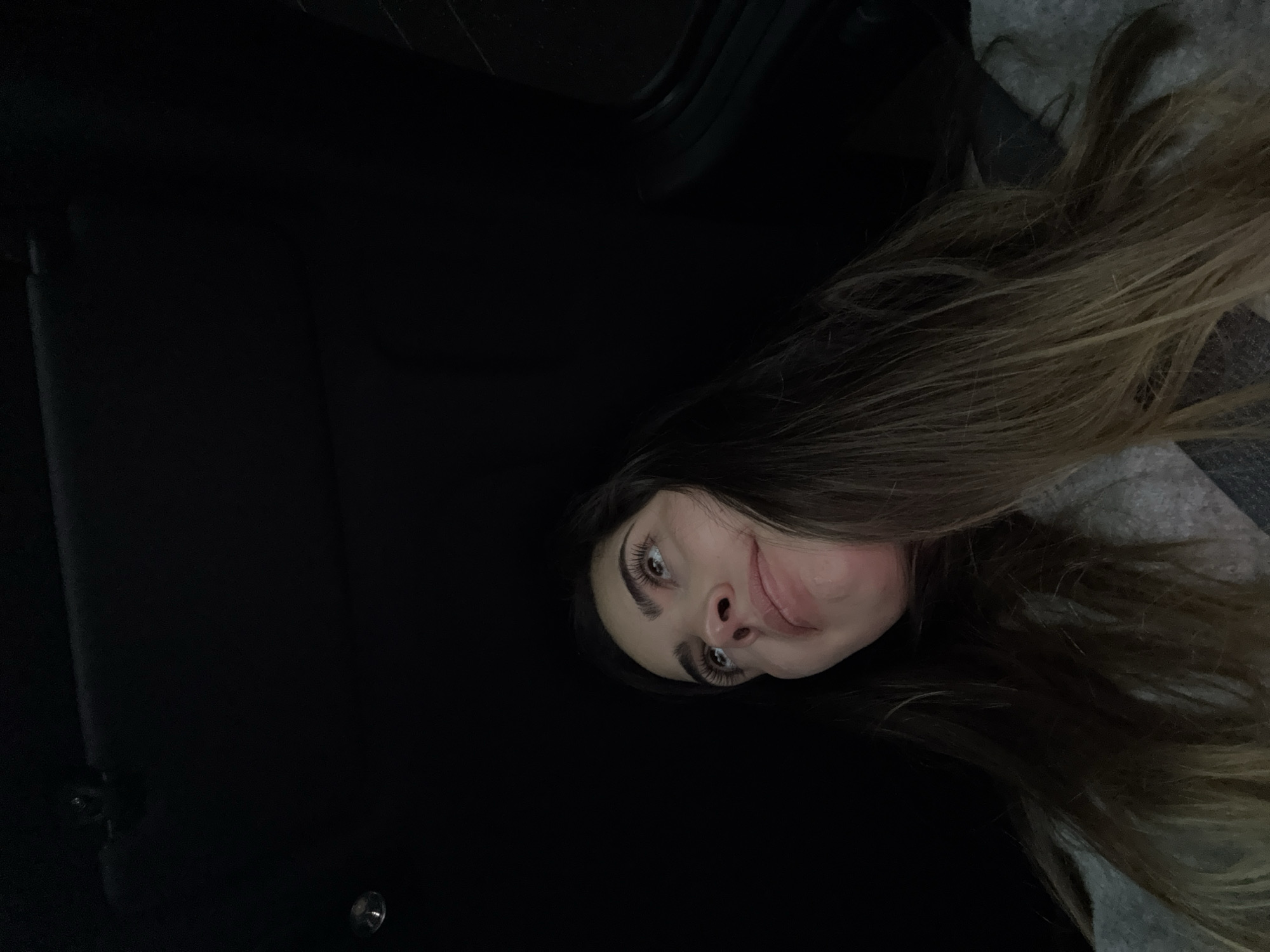 A woman with long, brown hair is positioned in the lower right of the frame, her face visible. She has fair skin, defined eyebrows, and light-colored eyes. Her expression appears neutral. The background is predominantly dark and out of focus. The location is not discernible from the image, therefore San Bernardino Tlaxcalancingo, Mexico is not confirmed.
