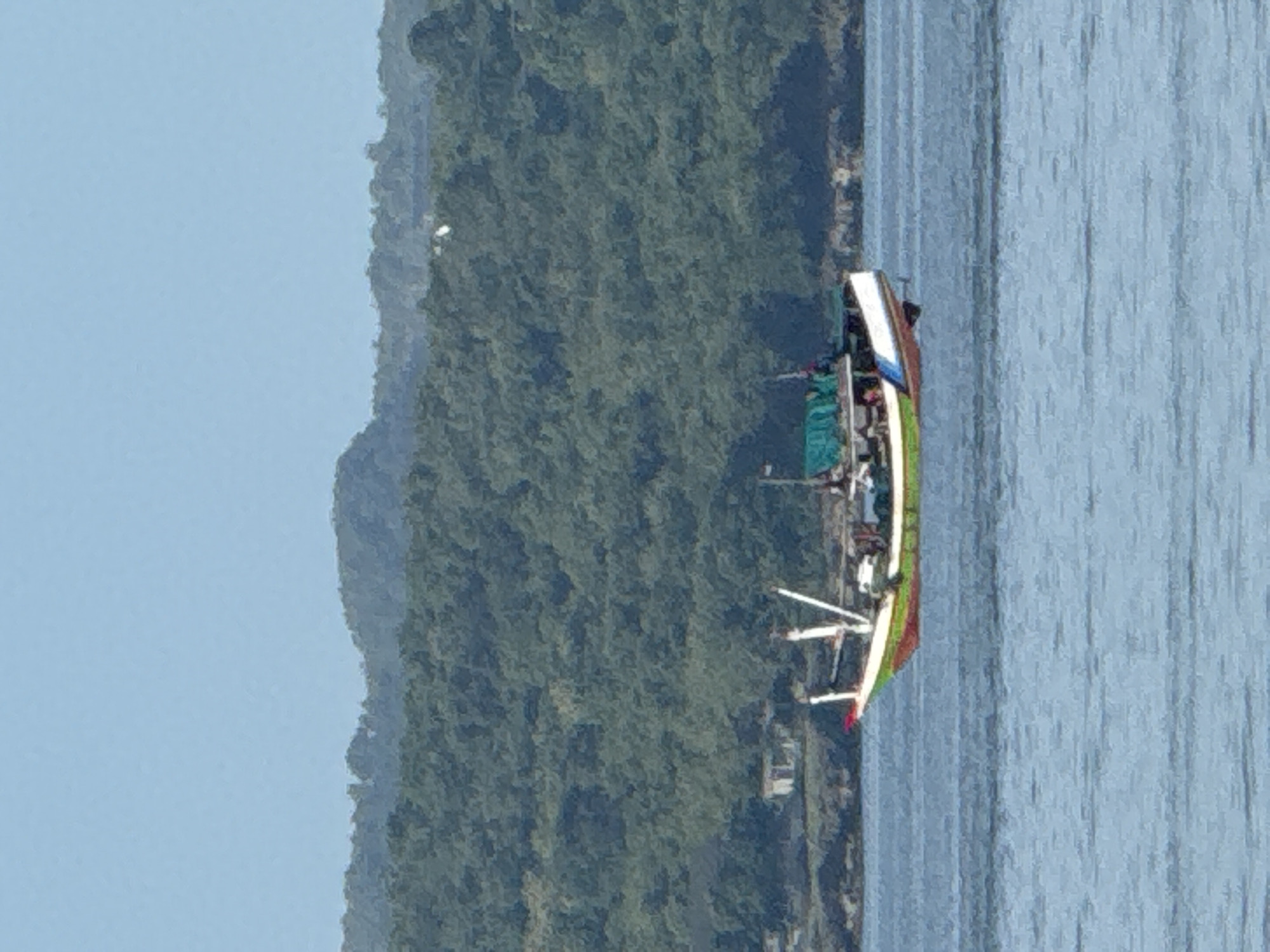 A boat is sailing on the water with land on the background. The location is likely near Denpasar, Indonesia, given the tropical vegetation visible.