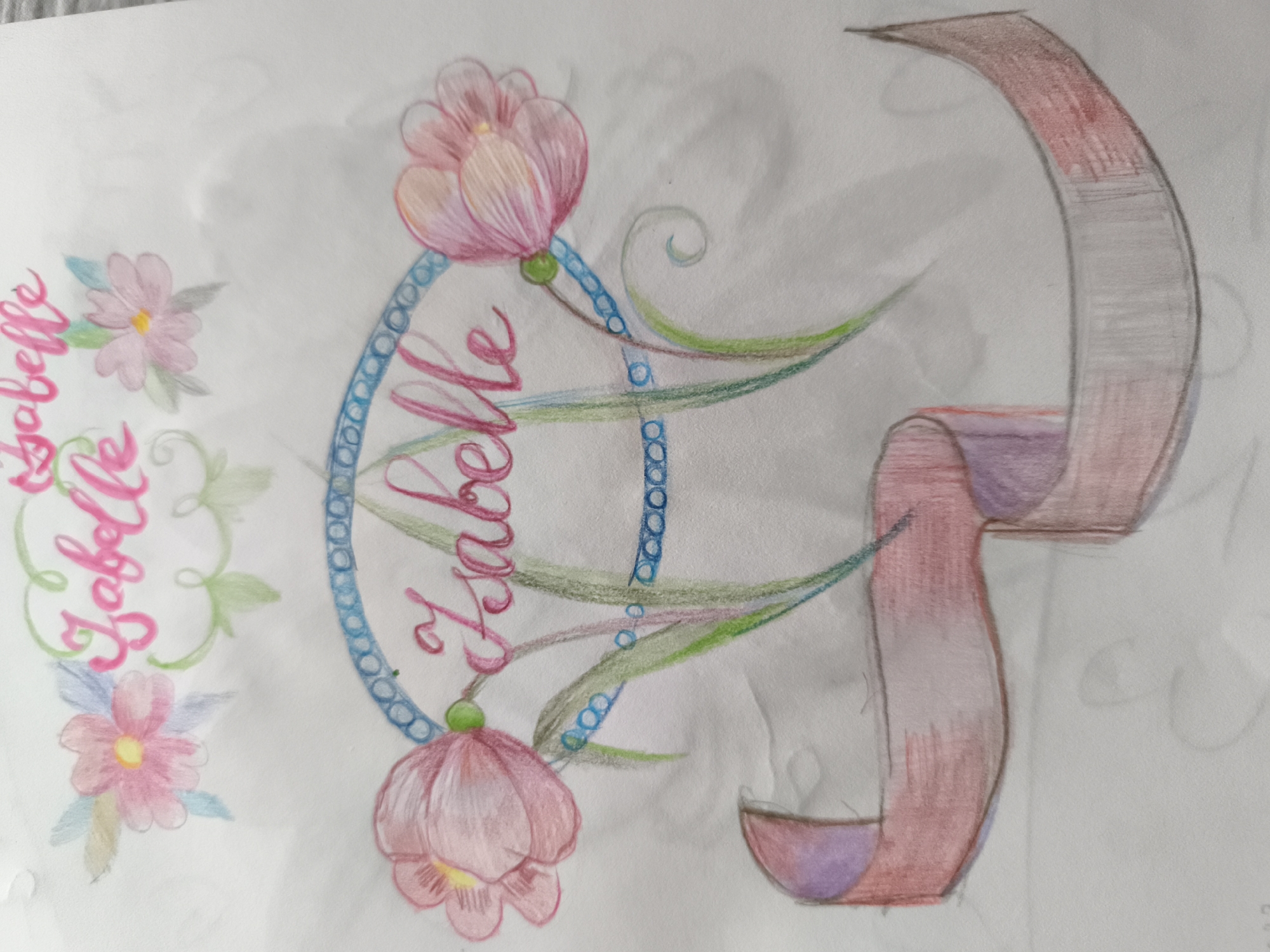 The image is a colored pencil drawing on paper. The drawing features decorative lettering and floral elements. On the left side, the name "Isabelle" is written in a cursive, pink font. To the right of the name are two stylized pink flowers with yellow centers, surrounded by green leaves and some blue accents. In the center of the drawing, a circular frame is depicted, outlined in blue with a beaded pattern. Inside this frame, the name "Isabelle" is again written, this time in a darker pink, more elaborate script, with a green accent dot above the "i". Swirling green lines emanate from the center, resembling leaves or vines. Two large pink floral blooms, similar to tulips, are attached to the bottom and top of the frame. To the right of the central design, a large, curved ribbon-like element is drawn in shades of red, grey, and purple, appearing to unfurl from the central design. The background is plain white paper, with some faint smudges and indentations visible. The drawing is rendered in a soft, illustrative style. There are no people or identifiable locations depicted in the drawing. The image is a creative artwork and does not represent a scene in Saint-Denis, France, or any other specific city.