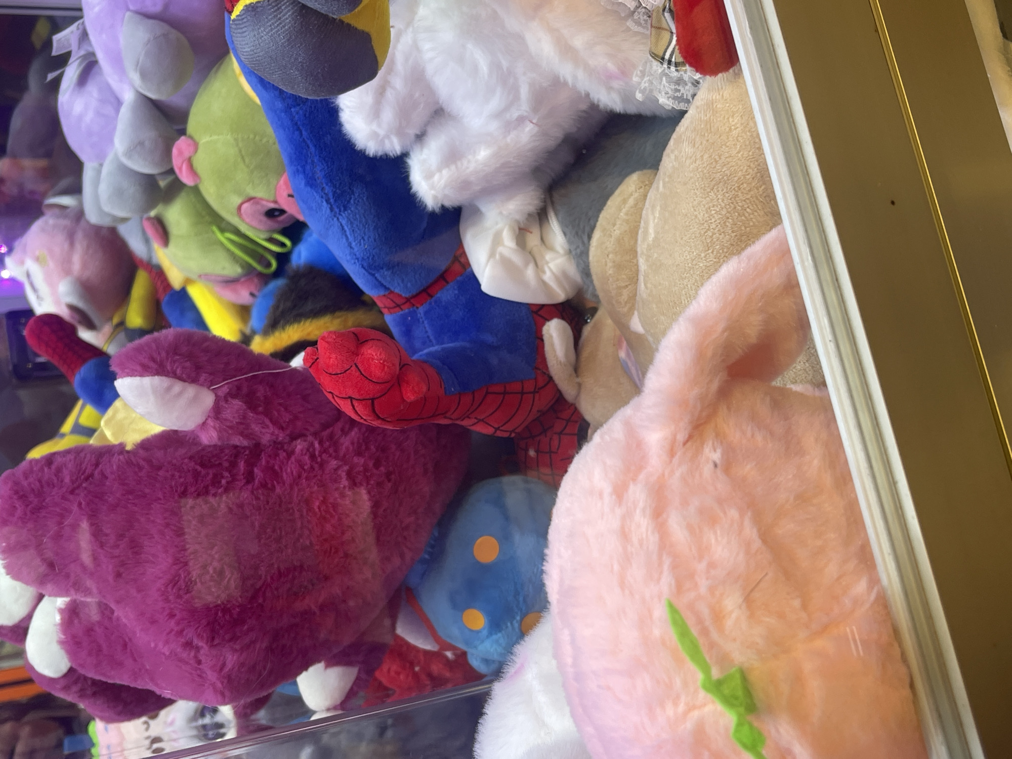 The image shows a close-up view inside a claw machine filled with stuffed toys. The toys include a purple monster, Spider-Man, a pink bunny, and several other plush figures in varying colors and shapes. The toys are tightly packed together, creating a chaotic jumble. The machine's glass panel and frame are visible. There are no visible people in the image. There is no verifiable information to suggest that this image was taken in Razvilka, Russia.