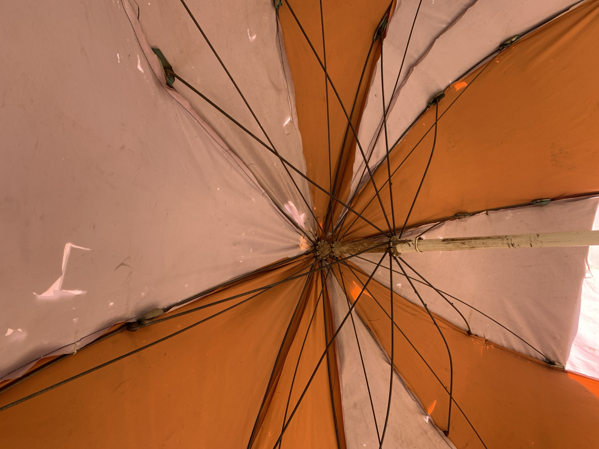 View looking up at the underside of an open orange and white parasol. The parasol's ribs and support pole are visible. The exact location in Rafin Par, Nigeria is not identifiable from the image.