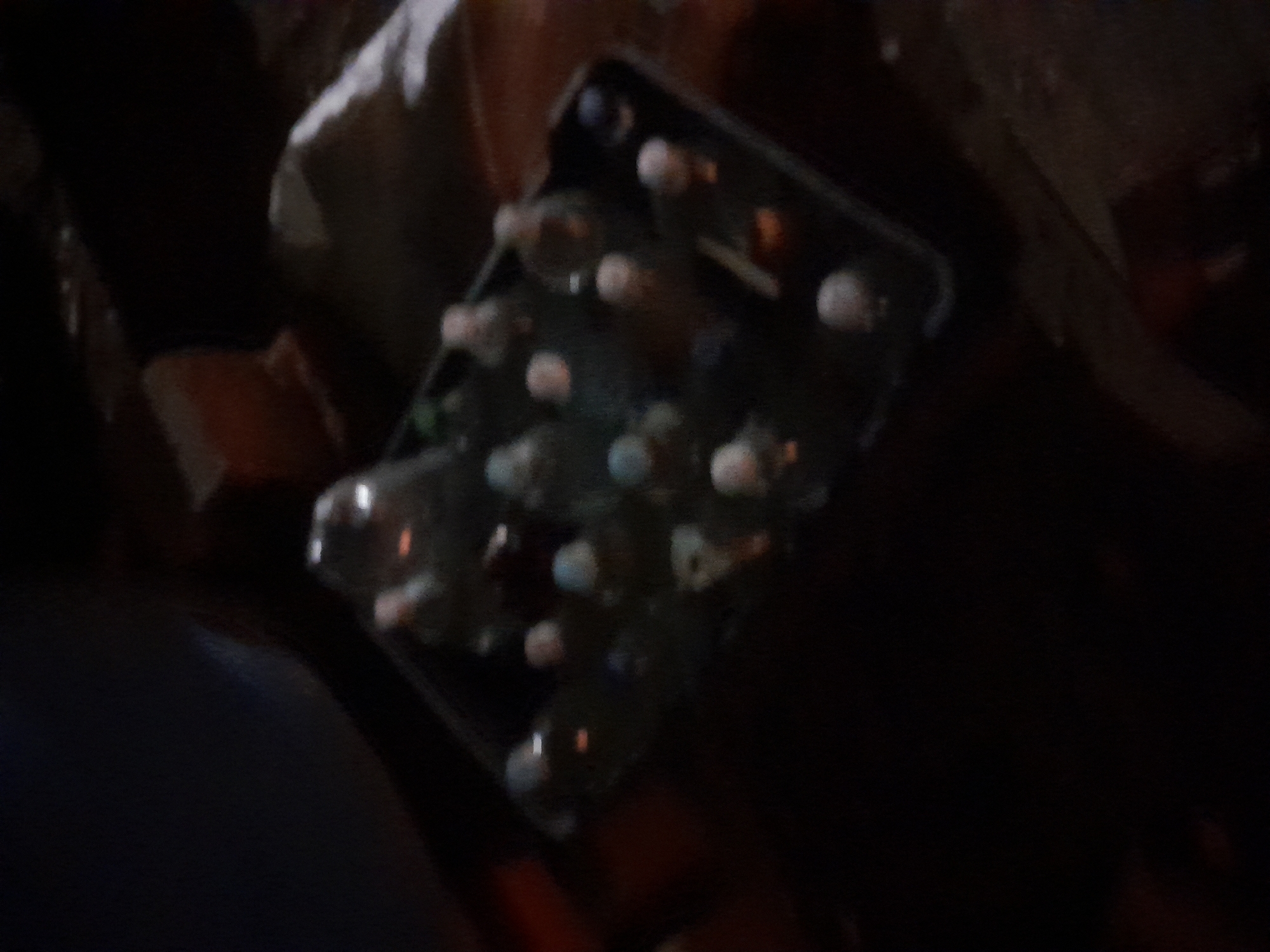 The image shows a dark, blurry scene, likely at night. In the foreground, a dark tray holds multiple clear plastic bottles, many with white or light-colored caps. Some bottles appear to be partially filled with liquid, while others may be empty. The bottles are arranged in a grid pattern within the tray. The background is indistinct but suggests an indoor or outdoor setting with dim lighting, possibly artificial. There are some reddish-brown rectangular objects visible in the background to the left and right. The overall impression is one of storage or transport of beverages. The location in Santa Ana, Venezuela, cannot be determined from the visual information provided.