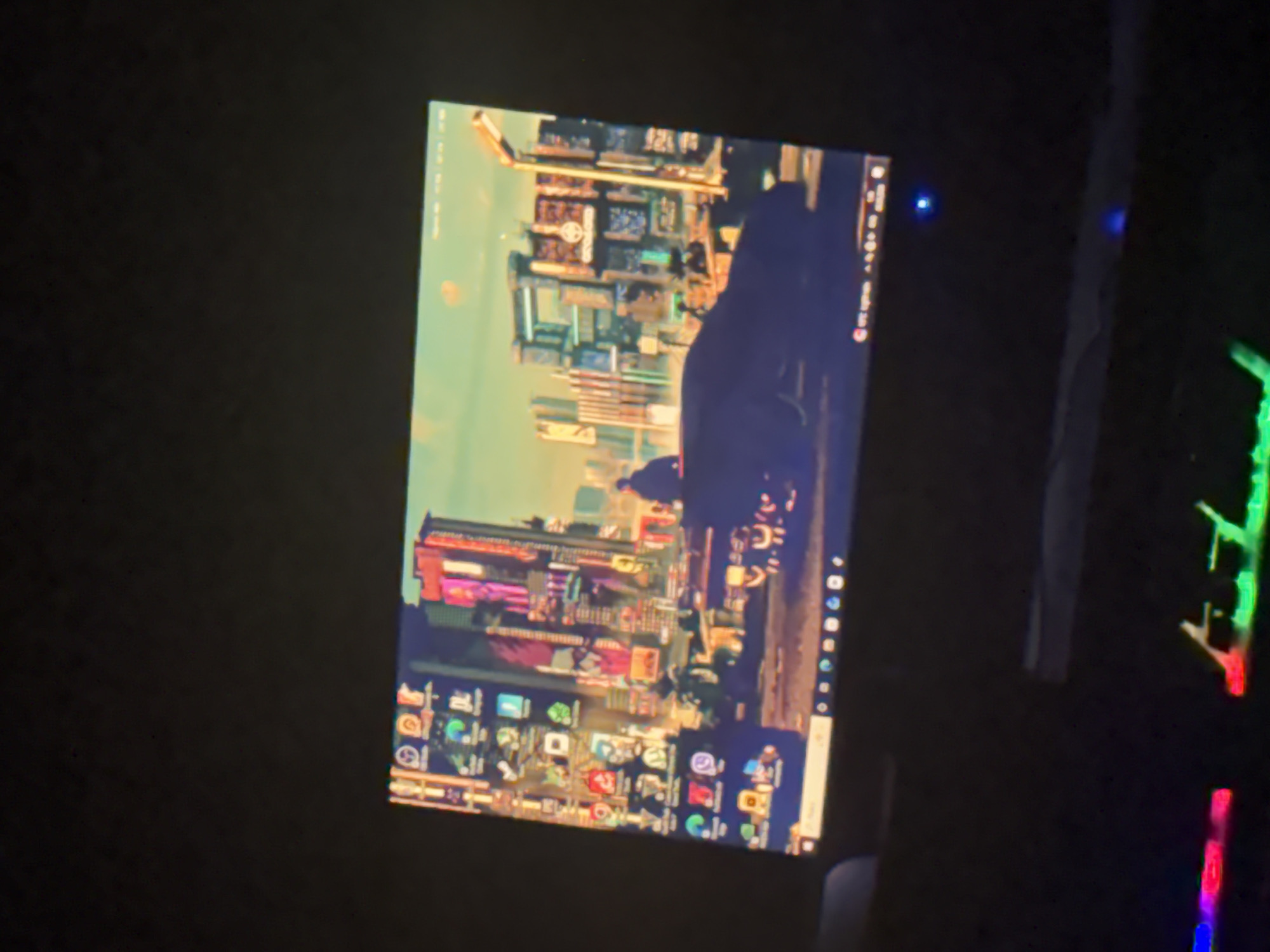 A computer monitor displays a cityscape wallpaper, featuring tall buildings, a vehicle, and a pedestrian. The monitor rests on a dark surface. Adjacent to the monitor, a partially visible keyboard exhibits colored lighting. The location is indeterminable.