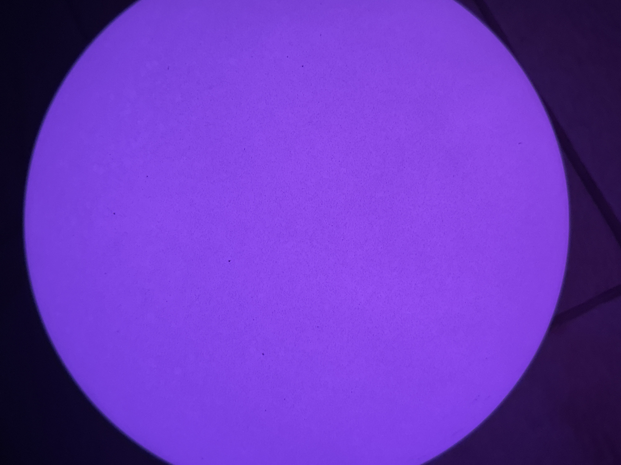 A close-up, overhead shot depicts a glowing purple sphere. The sphere occupies most of the frame, and its surface appears slightly textured. The background is a dark, indistinct surface that contrasts sharply with the bright sphere. It's impossible to ascertain location based on visual data. No people, subjects, actions, or interactions are discernible. The image contains only the illuminated sphere and an indeterminate background.