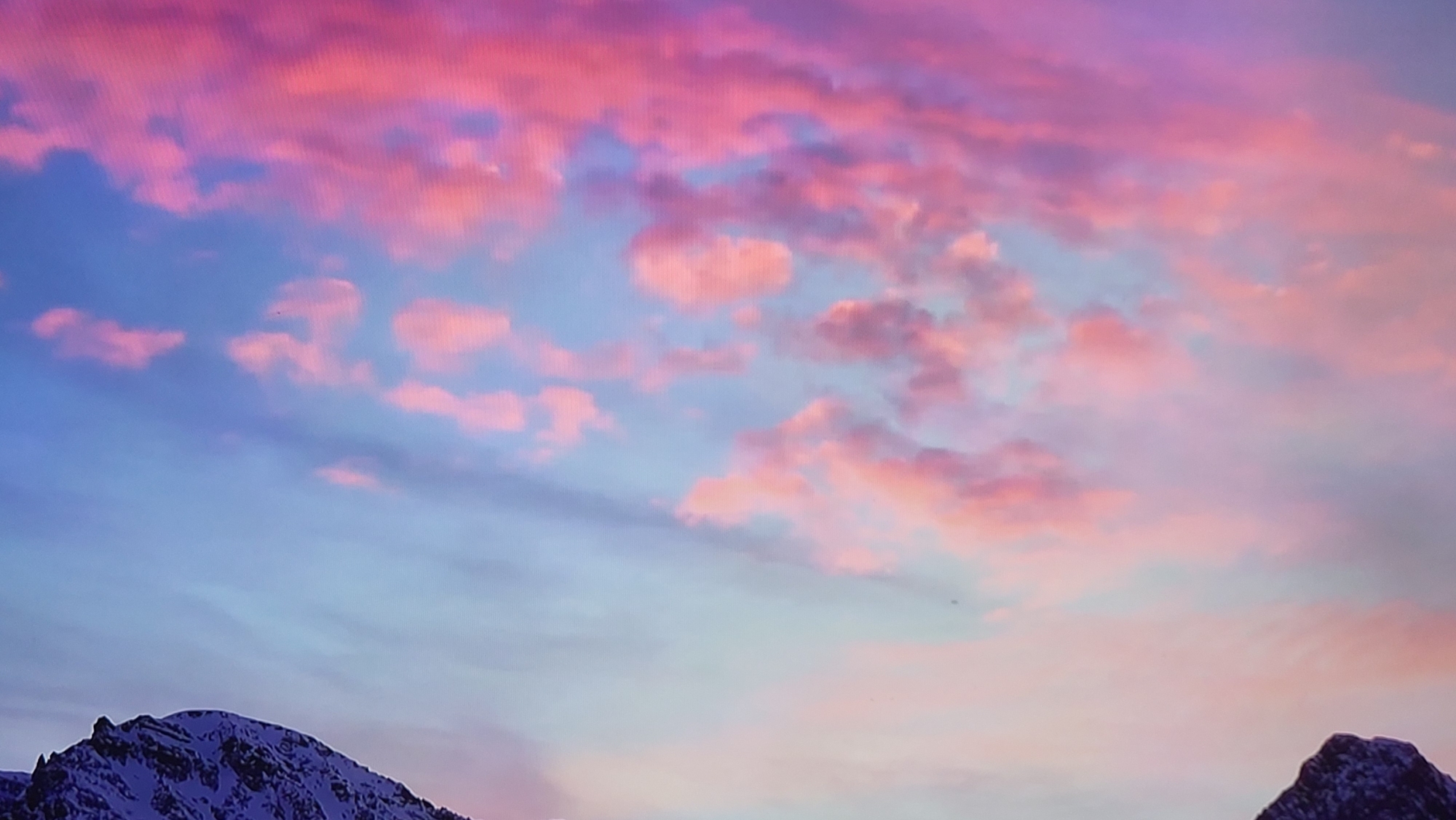The image depicts a scenic view of snow-capped mountains under a sky with pink and blue hues. The sky is filled with a mix of blue sky and pink clouds, suggesting either sunrise or sunset. The mountains are visible in the foreground, covered with snow. The location of Yerevan, Armenia is not confirmed.