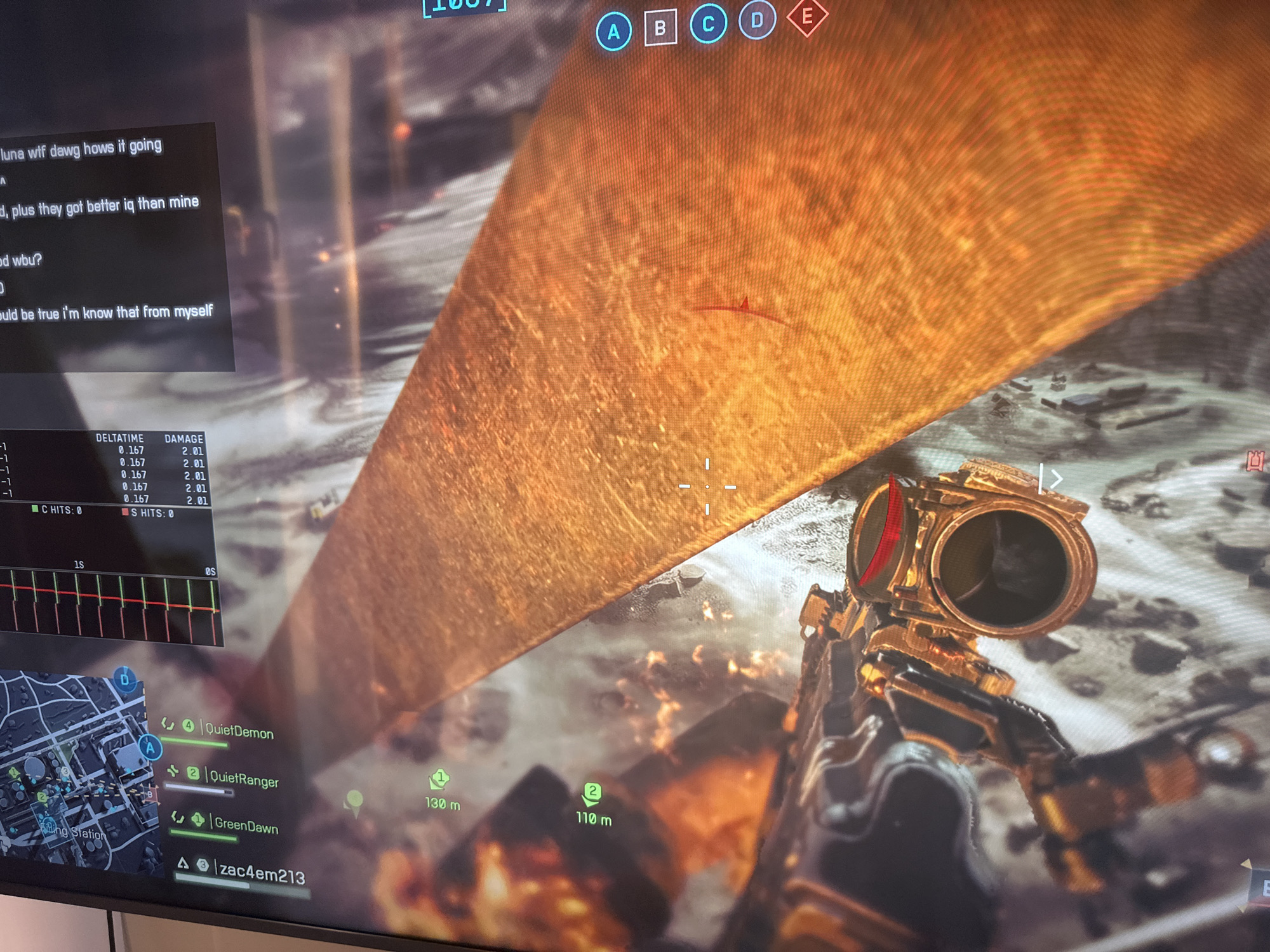 A first-person perspective screen capture of a video game, likely a first-person shooter, shows a player holding a gold-colored rifle with a red-accented scope. The player is looking towards a massive, reflective golden-brown structure or terrain feature that dominates the upper and central parts of the screen. The ground below appears desolate and rocky, with visual effects suggesting fire or explosions.
The game's heads-up display (HUD) is prominent, featuring various elements. At the top, objective markers 'A', 'B', 'C', 'D', 'E' are visible, with 'A' and 'E' highlighted in blue and red respectively. The top left corner displays a partial score of "1007". In the upper left, a chat window contains text such as "luna wtf dawg hows it going", "plus they got better iq than mine", "od wbu?", and "would be true i'm know that from myself".
Below the chat, a performance overlay shows "DELTATIME" and "DAMAGE" statistics, consistently listing "0.167" and "2.01" values, along with "C HITS: 0" and "S HITS: 0". A small graph with red and green lines is also visible. The lower left features a minimap centered on "Long Station" with objective points. On the right side of the screen, two objective markers show distances of "130 m" and "110 m". A player list in the lower left includes names like "QuietDemon", "QuietRanger", "GreenDawn", and "zac4em213". The overall scene depicts an active moment within a multiplayer gaming session.