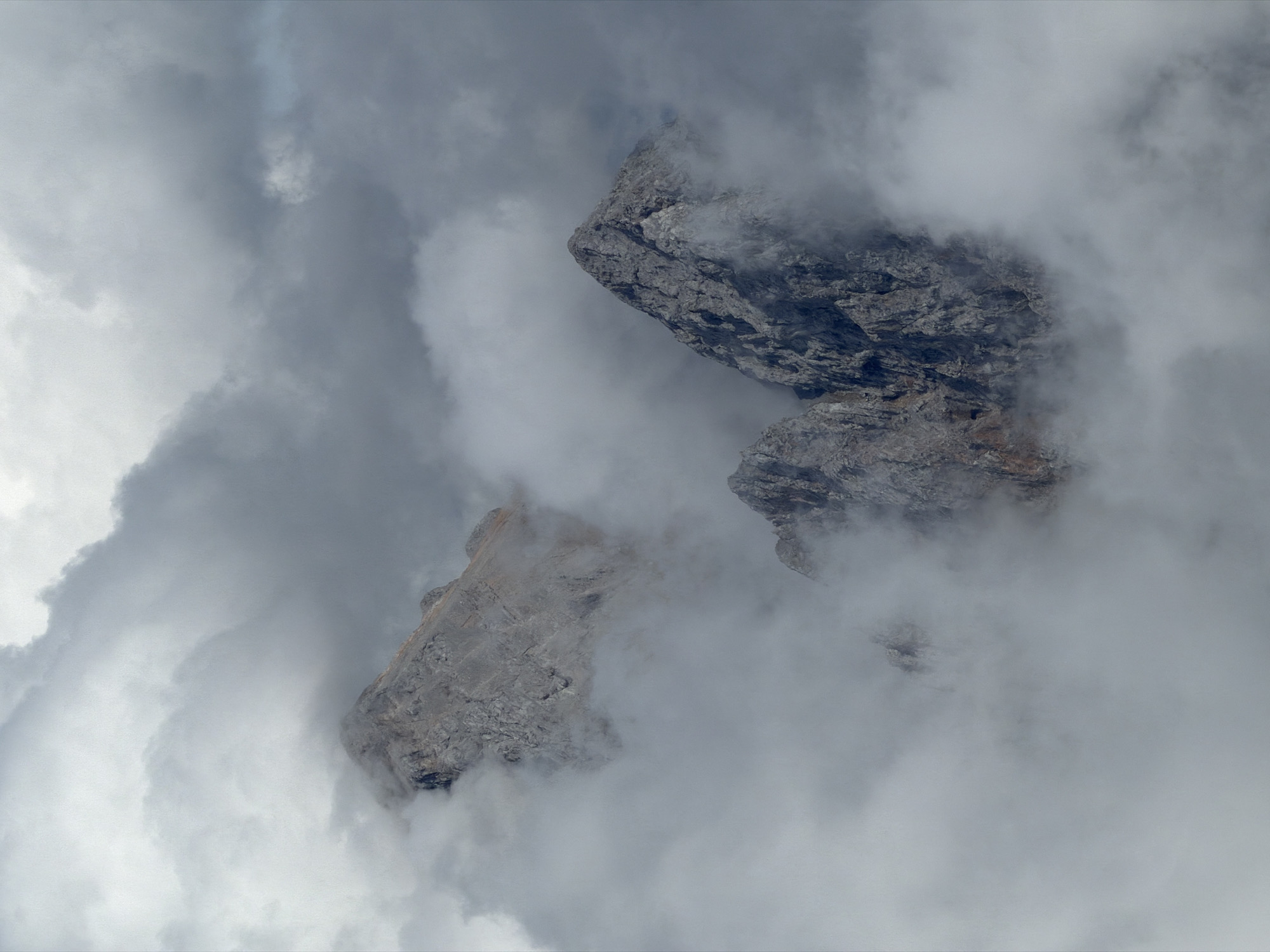 The image depicts a dramatic view of mountain peaks emerging from a sea of clouds, evoking a sense of grandeur and remoteness. The composition is dominated by shades of gray and white, with the rugged texture of the rock faces contrasting against the soft, ethereal quality of the fog. The lighting is diffused, suggesting an overcast or misty day, which enhances the dramatic atmosphere.
While the image strongly suggests a mountainous region, and the prompt mentions Garmisch-Partenkirchen, Germany, it is impossible to definitively confirm this specific location based solely on the visual information provided. Garmisch-Partenkirchen is known for its alpine scenery, including mountains like the Zugspitze, which share a similar rugged, cloud-shrouded appearance. Therefore, the scene is consistent with the natural environment found in such a location.
There are no people, animals, or man-made structures visible in the image. The focus is entirely on the natural landscape: the imposing rock formations and the enveloping clouds. The environment is one of high altitude, characterized by steep, rocky terrain and significant atmospheric moisture. The perspective is from a vantage point that looks down upon or amongst the peaks, emphasizing their scale and the enveloping nature of the fog.