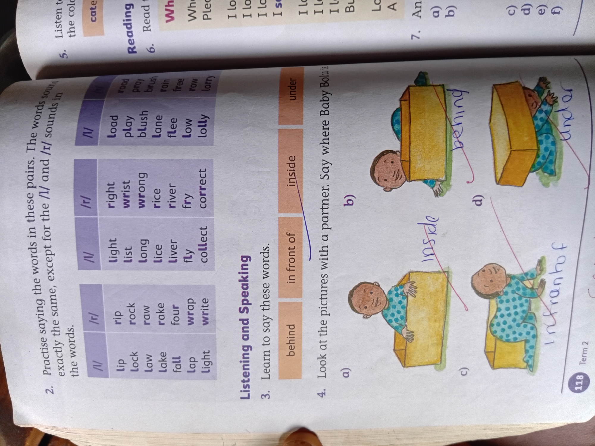 The image displays two pages of a children's educational book, focusing on language and reading exercises. The left page has a section titled "Practise saying the words in these pairs," which is followed by a table of words categorized by their initial sounds, specifically "/l/" and "/r/". Below this, there's a "Listening and Speaking" section with instructions to "Learn to say these words" and provides three options: "behind," "in front of," and "inside." The page also includes an activity labeled "Look at the pictures with a partner. Say where Baby Bolu is," featuring four illustrations (labeled a, b, c, and d) of a baby in and around a box, with handwritten answers indicating the baby's position: "inside," "behind," "in front of," and "under." The bottom left corner shows the page number "118" and "Term 2."
The right page contains a "Listen to..." instruction and a section on "Reading," with a prompt for question 6: "Read th". This is followed by a "What..." section and then question 7: "Ans". The image also contains what appears to be a partial answer written in blue marker pen next to illustration "a)" on the left page.
The overall environment is a printed book, likely found in a classroom or home setting. There are no discernible elements that would place this image in Nkpor, Nigeria; it is a generic educational material.
