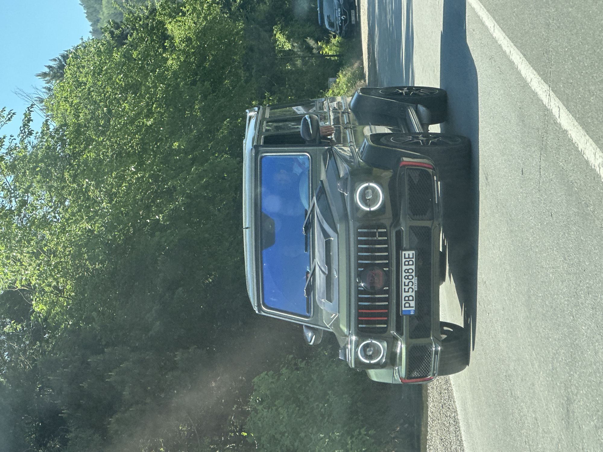 The image shows a dark-colored Mercedes-Benz G-Class SUV with a Bulgarian license plate "PB 5588 BE" driving on a road. The car is facing the camera and slightly to the left. The road appears to be asphalt. In the background, there are green trees, suggesting the vehicle is in a natural, possibly rural or suburban, environment. There is no other prominent information available that provides insight regarding the location of the city of Veliko Tarnovo, Bulgaria.