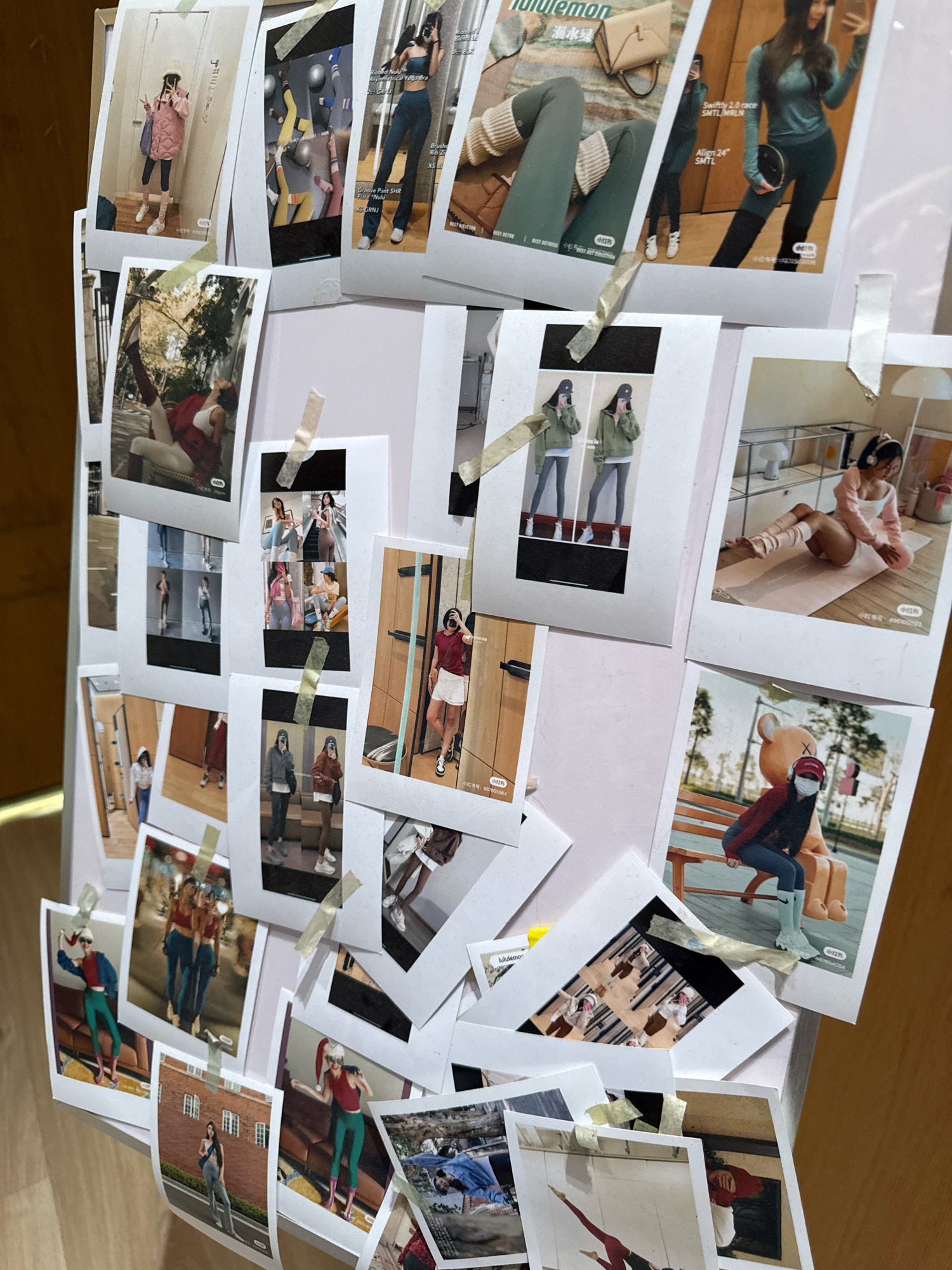 The image displays a collection of photographs, predominantly featuring women in athletic wear, taped to a white board. The photographs appear to be a mix of candid shots and posed product imagery, possibly related to activewear brands. Some images show individuals in gym settings, while others are taken outdoors or in what seem to be retail environments. There is no visible indication of the city of Yiwu, China in the image or its contents. The overall arrangement suggests a mood board or a personal display of fashion inspiration.