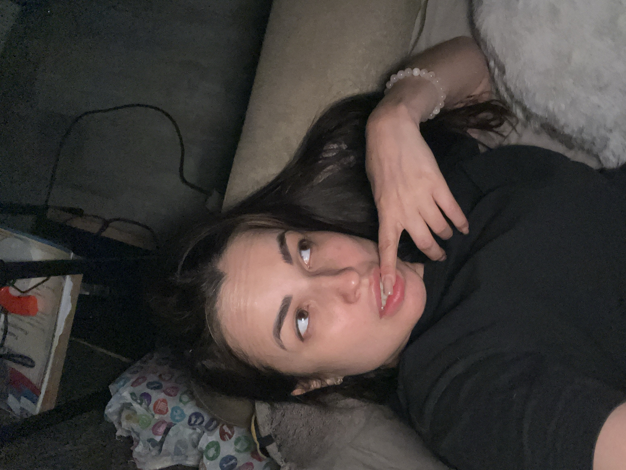 A woman is lying on a couch, wearing a black top and a bracelet. Her left hand is near her mouth. A blanket is next to her. The location in the city is unknown.