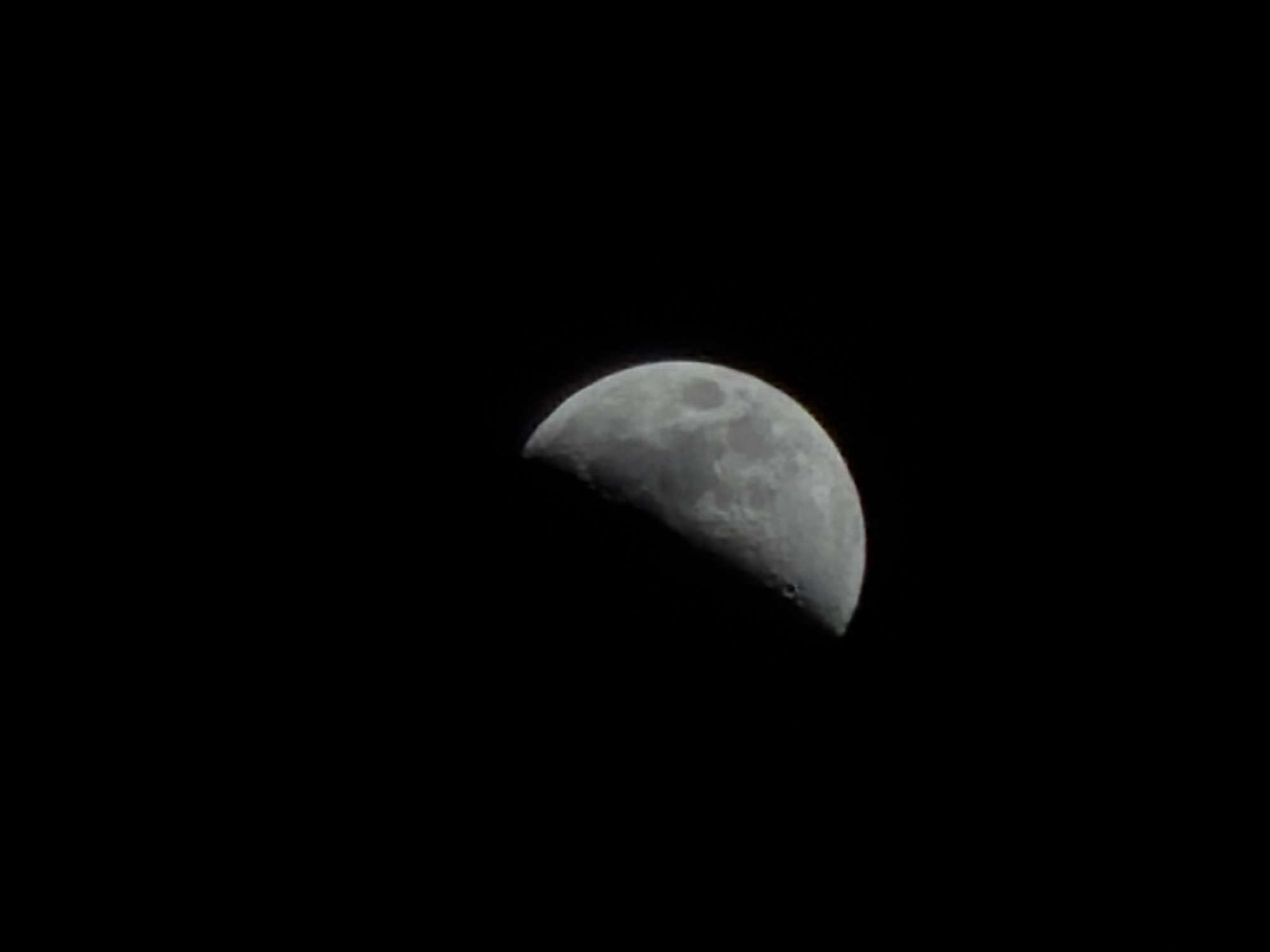 The image shows a waxing crescent moon in a dark, presumably nighttime, sky. The visible portion of the moon is grayish-white and textured with craters and other surface features. The rest of the image is uniformly black, representing the night sky. There is no information in the image that indicates a location in Izhevsk, Russia, or any other place.