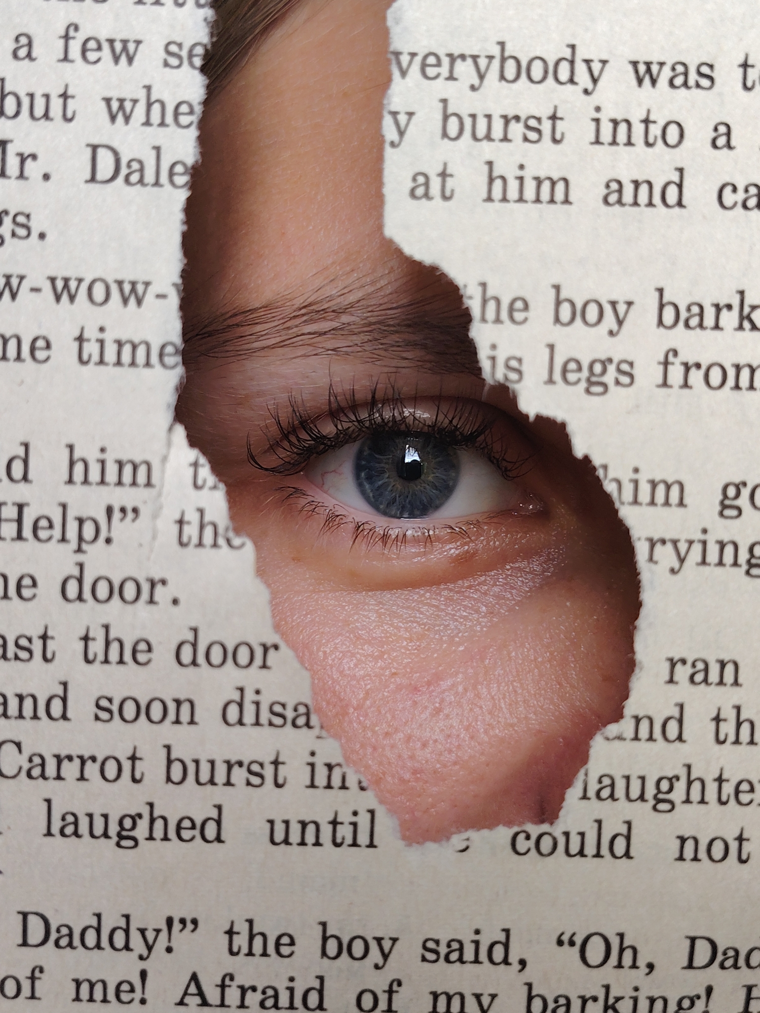 A close-up, eye-level shot features a human eye peeking through a torn section of a book. The eye is bright blue with long, dark eyelashes. The skin surrounding the eye is a light, peachy tone with visible pores and some texture. The torn book pages reveal printed text, partially obscured by the skin. The lighting appears to be natural, casting soft shadows and highlighting the texture of the skin and the paper. There is no information about the location of Chaikovsky, Russia in this image.