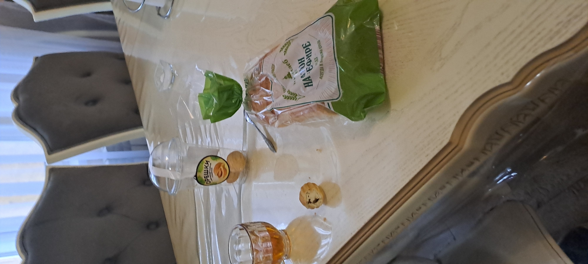 A table in Yekaterinburg, Russia, holds a package of bread, a plastic cup of "Oreshki" cookies, a spoon, a small pastry, and a partially full glass of liquid. Two upholstered chairs are visible to the left.