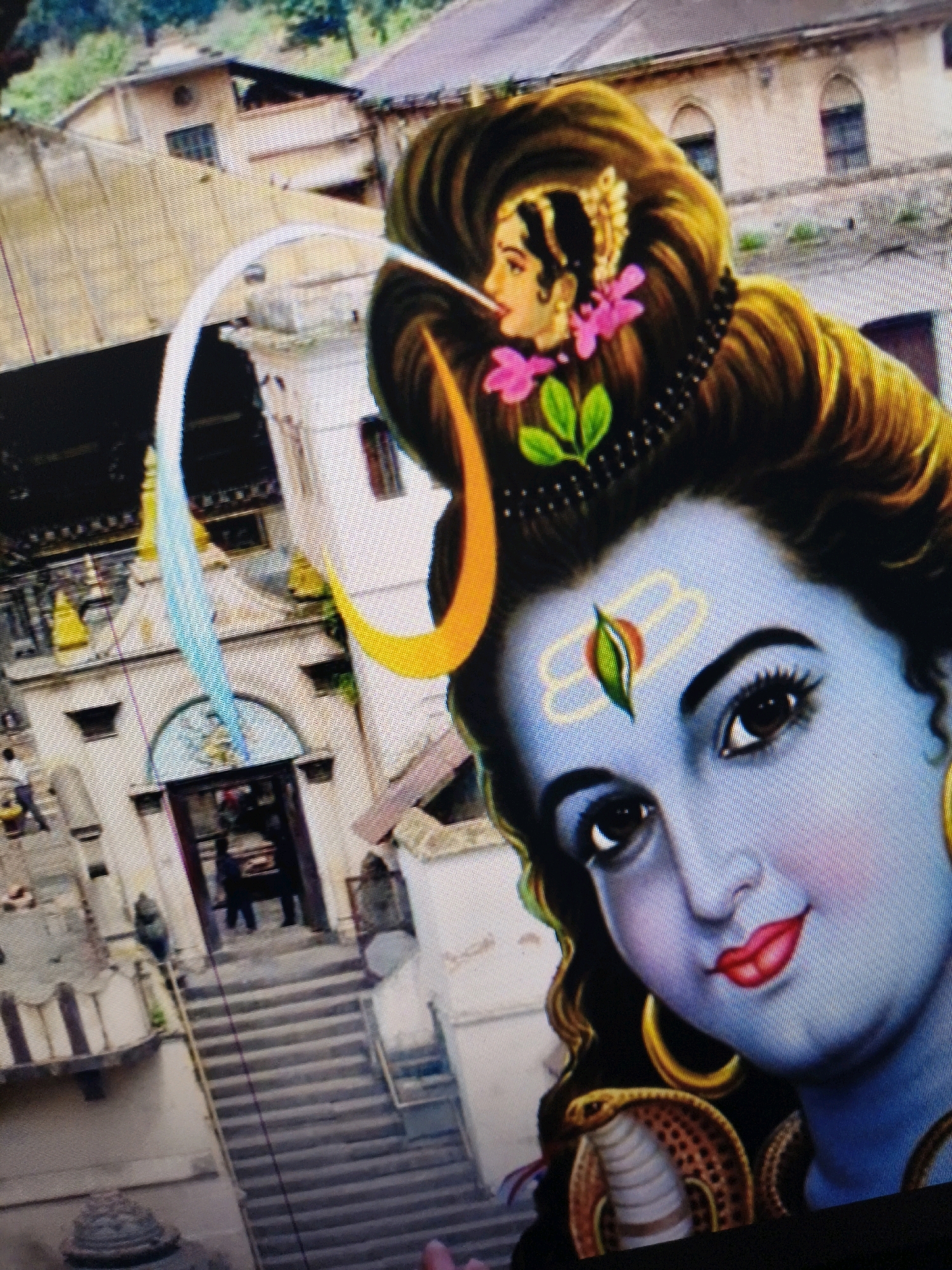 The image depicts a close-up of a stylized portrait of a deity with blue skin, adorned with elaborate hair, a third eye on the forehead, and a snake around the neck. The background shows a temple complex with stairs and buildings, appearing to be a religious site in Ratnanagar, Nepal. Several indistinct figures are visible in the background, some climbing the stairs or standing near the entrance of the temple. The overall composition is tilted, with the deity's face dominating the foreground.