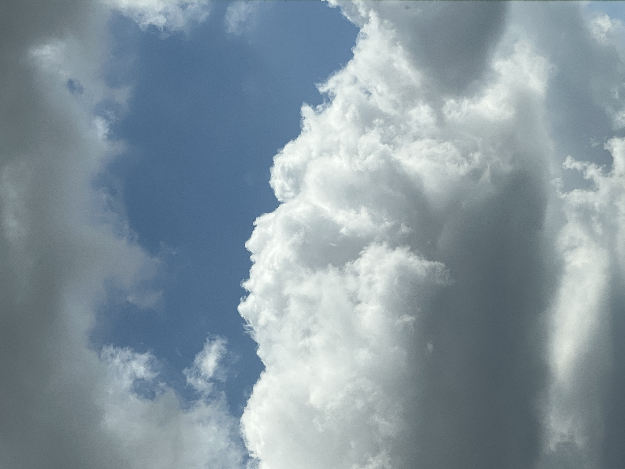 A low-angle shot captures a sky filled with a mix of fluffy white cumulus clouds and darker, grayer clouds. The blue sky is visible through patches of the clouds. The scene is a natural outdoor environment. There are no people, subjects, objects, or actions depicted in the image. The location is identified as Warsaw, Poland.