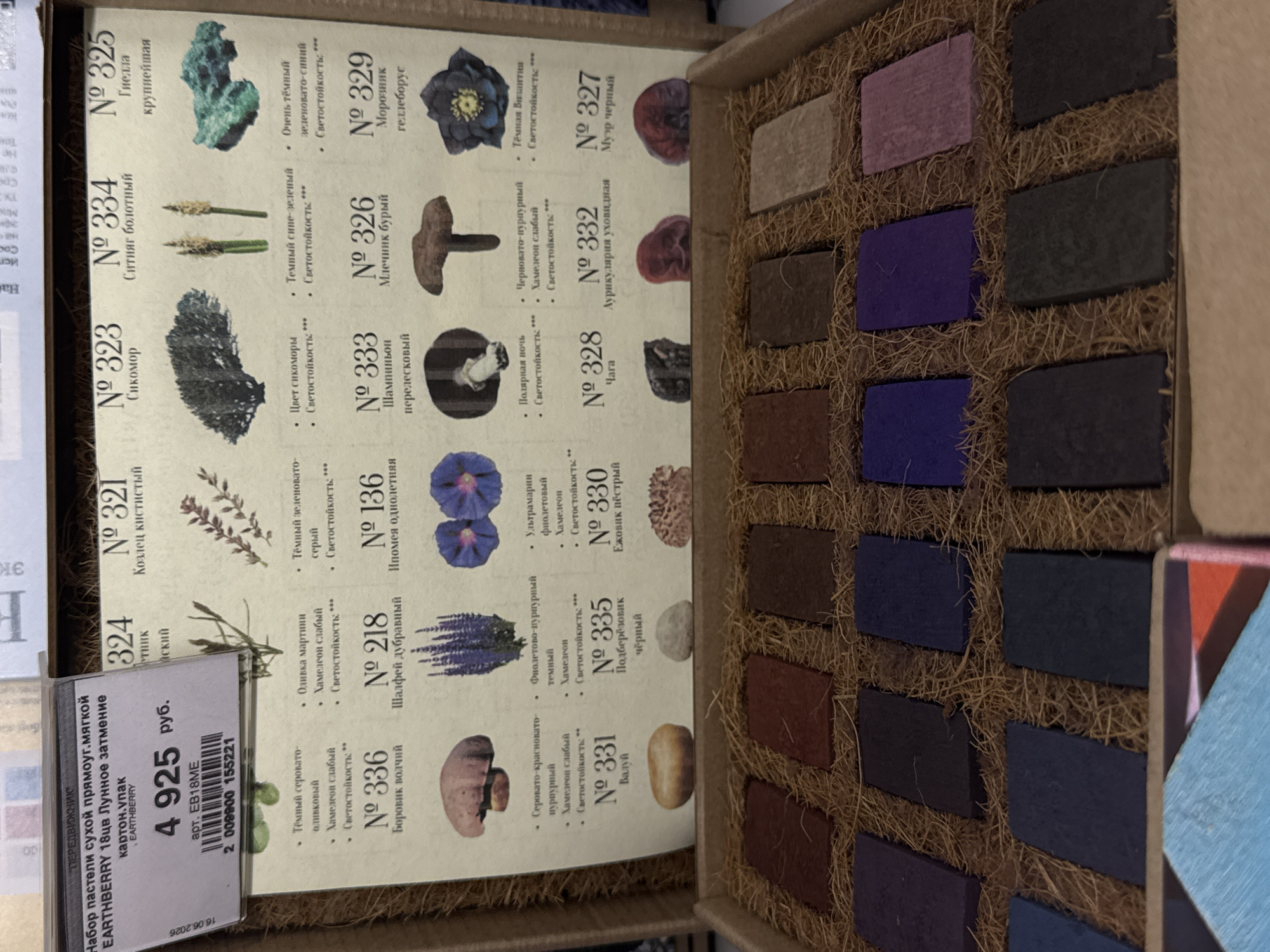 The image shows a close-up of a product display for "EARTHBERRY 18ub Лунное затмение" (EARTHBERRY 18ub Lunar Eclipse) dry pastels in the city of Moscow, Russia. The display features a set of numbered pastels, each with a corresponding illustration of a plant or mushroom and a description. The price is clearly visible as 4925 rubles. Below the product display, the pastels themselves are arranged in compartments within a box, showcasing their colors. The overall presentation suggests a retail or exhibition setting.