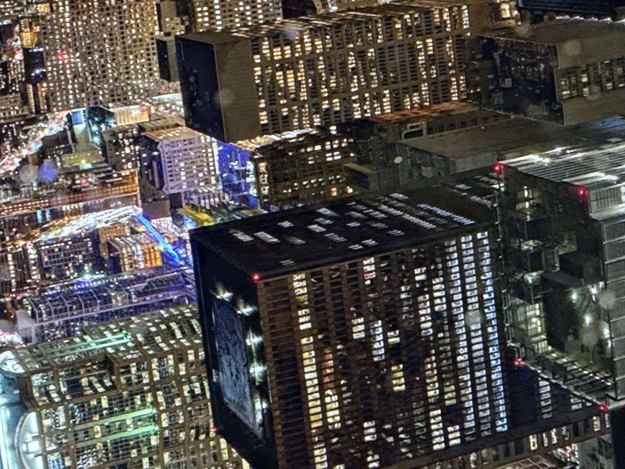 The image is an aerial view of a dense urban landscape at night, characterized by numerous illuminated skyscrapers. The buildings vary in architectural style and height, with windows glowing from within, suggesting occupied office spaces or residences. Some buildings are clad in glass and metal, reflecting the lights of other structures, while others appear to be older, with more traditional facades. Light trails from traffic are visible in the distance, indicating a bustling city environment. The perspective is from a high vantage point, looking down and across the city.
The location of Saratov, Russia, is not discernible from the visual elements present in the image. The architecture and urban planning are not specific to any particular city, and there are no geographical markers or cultural indicators that would allow for such a determination. The scene depicts a generic modern city skyline at night. There are no discernible people or specific actions occurring within the image. The focus is on the architectural structures and the interplay of light and shadow across the urban expanse.