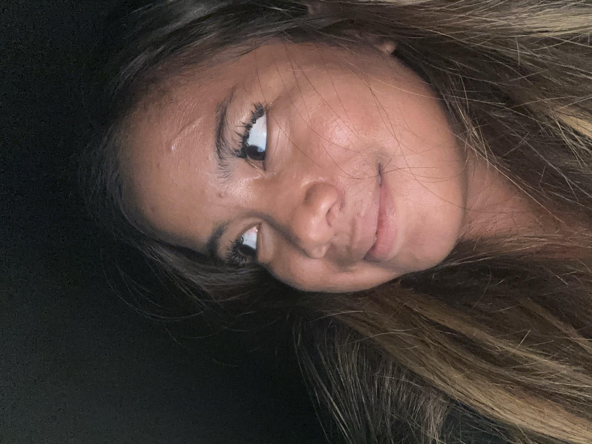 A close-up, rotated shot features a person with brown and blonde hair, and tan skin. The person is looking up and to the left with a slight smile. The background is dark and out of focus. There is no information in the image to determine its location in North Jakarta, Indonesia.