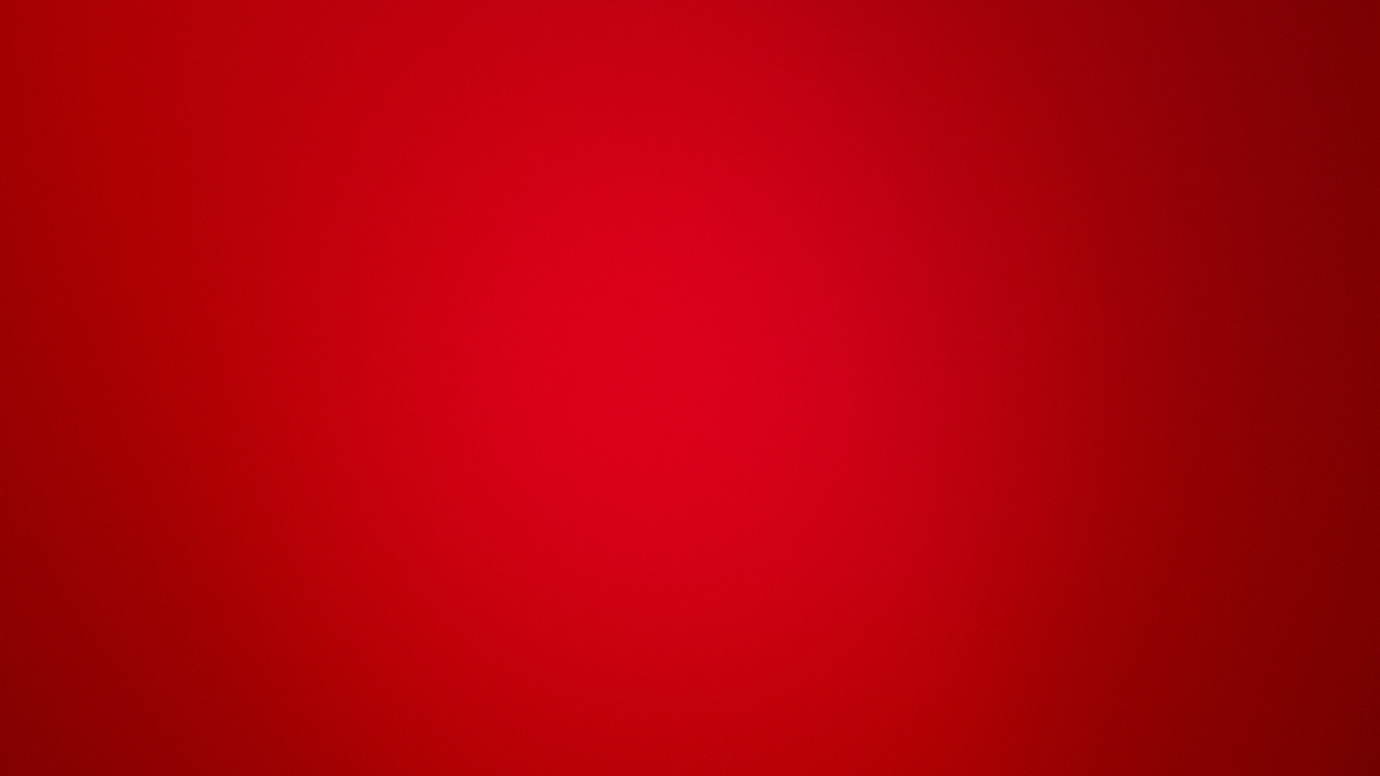 The image depicts an abstract scene located in the city of Unknown, Unknown. The primary subject is a smooth, vertical color gradient featuring shades of red. The upper and central areas of the frame display a brighter, lighter red, which gradually transitions to a deeper, darker red towards the bottom and edges. The gradient is subtle and uniform, lacking any distinct patterns, textures, objects, figures, or text. No actions or interactions are visible, as the scene consists solely of the color transition.