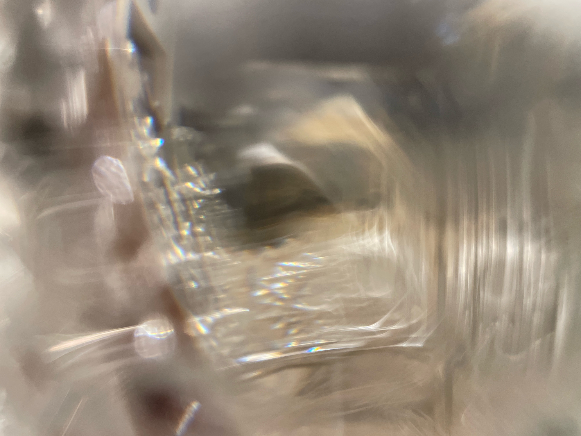 The image is an abstract close-up of light refracting through a transparent material, possibly glass or ice. It displays a spectrum of colors, streaks of white light, and blurred shapes. There is no discernible location in Cairo, Egypt, or any identifiable people, subjects, or specific objects. The scene is purely an effect of light and material properties.