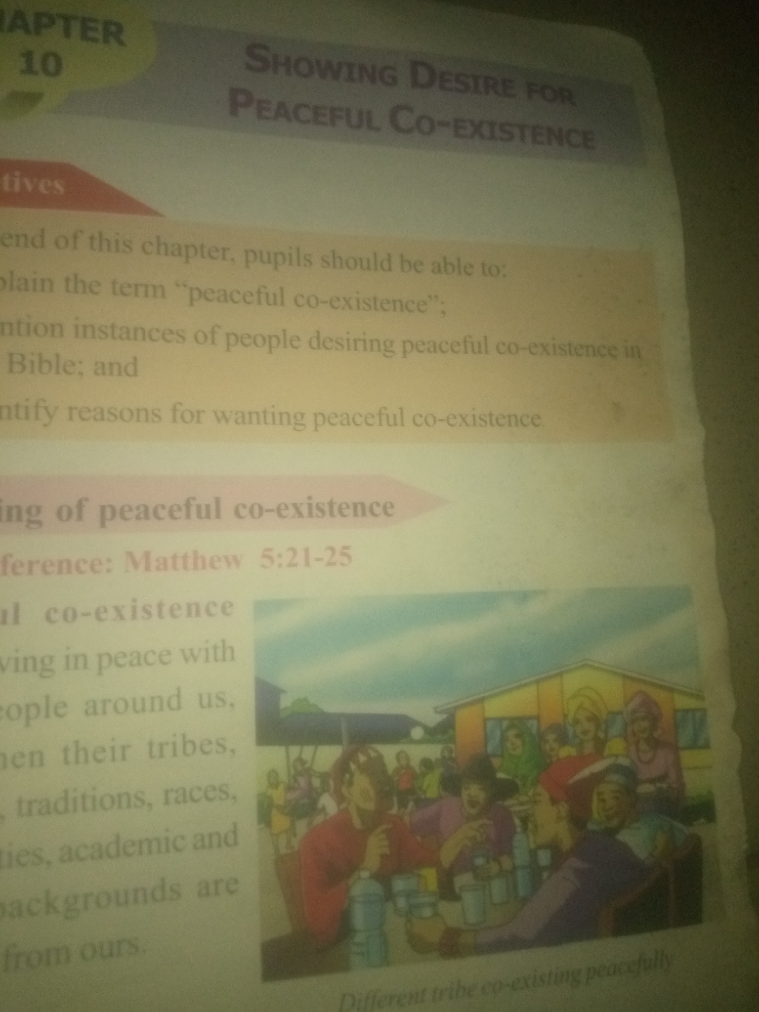 The image is a close-up of a page from a book or magazine, featuring text and an illustration. The text is in English and discusses "Peaceful Co-Existence." It appears to be an educational or religious text, with a reference to "Matthew 5:21-25." The illustration depicts a group of people from diverse backgrounds gathered together, seemingly in a friendly or celebratory setting, with a building in the background. The image does not contain any information or visual elements that indicate a specific location in Jauro Yinu, Nigeria.
