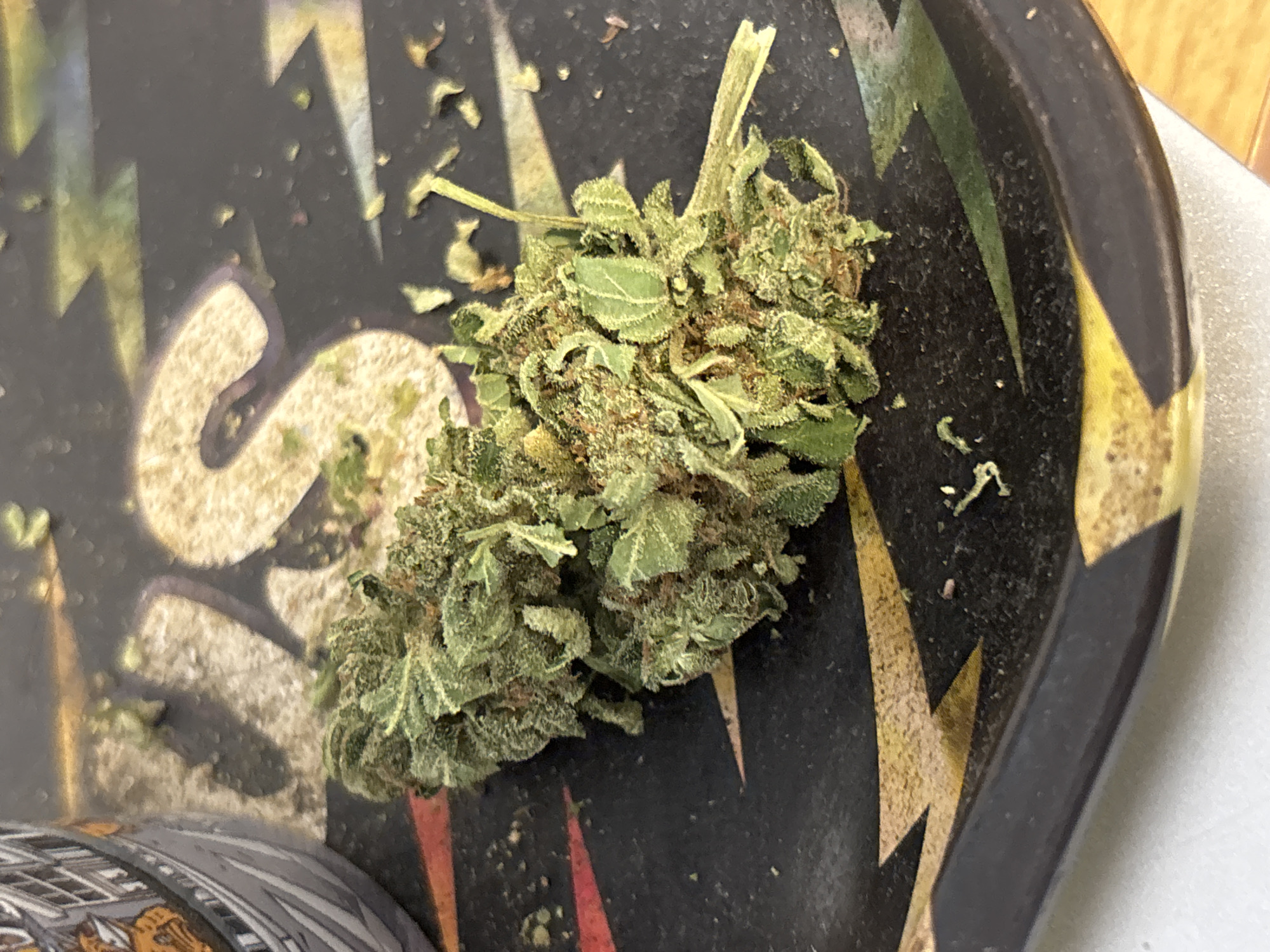 A close-up shot shows a cannabis bud on a black rolling tray. The tray has a colorful design with geometric shapes and lightning bolt patterns. The cannabis bud is green and appears to be trimmed. The background includes parts of other objects and a white surface. The specific location in Buenos Aires, Argentina, is not identifiable from the visual information.