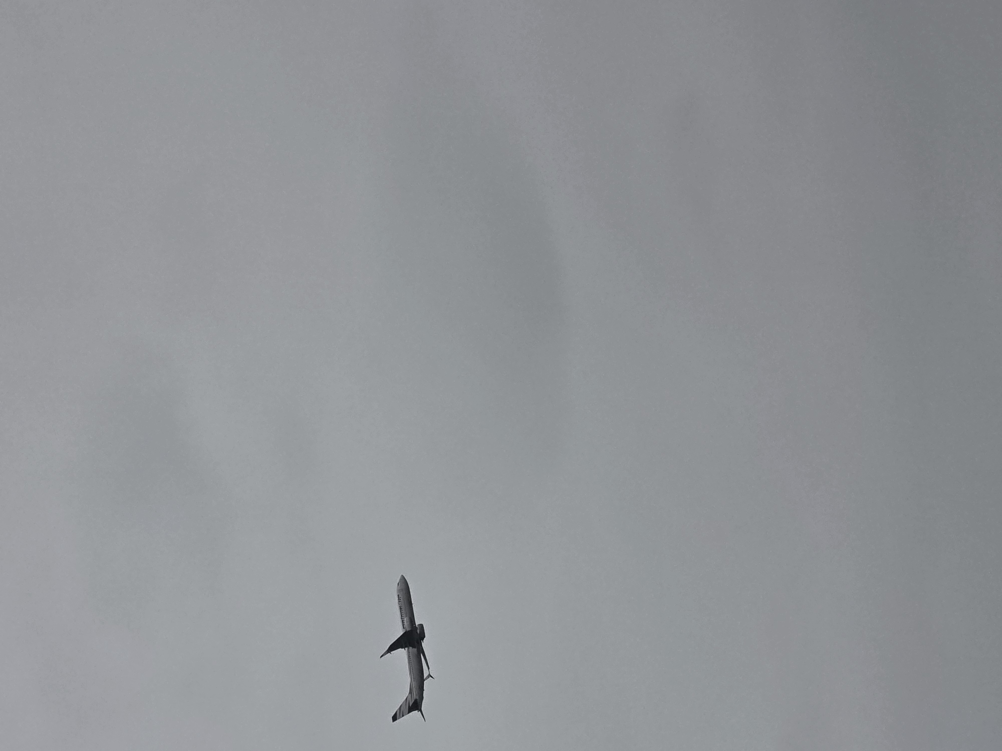 An airplane is captured in flight against a backdrop of overcast skies. The aircraft appears to be a commercial jet, with its wings extended and its body oriented horizontally. The image provides a clear view of the airplane's silhouette, with no discernible details of its livery or markings due to the distance and lighting conditions. The sky is a uniform shade of gray, indicating a cloudy day. The location in Poprad, Slovakia, is not visible in this image, as the frame is entirely occupied by the sky and the airplane.