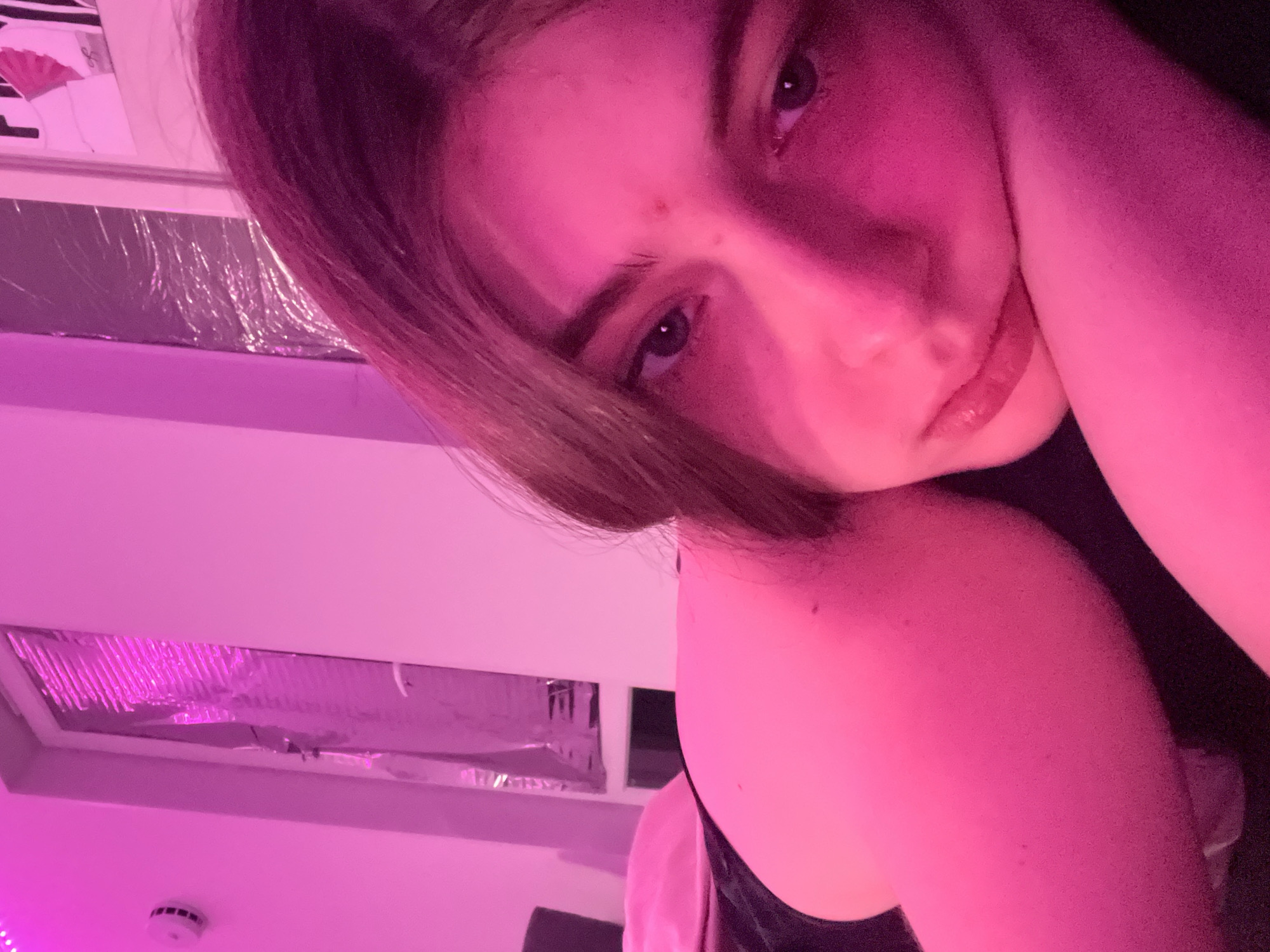 A close-up, angled shot under pink lighting features a person with short, brown hair and fair skin. Their head rests on their hand. The individual's gaze is directed toward the camera. A ceiling with a rectangular light fixture covered in reflective material is visible in the background. A smoke detector is also visible on the ceiling.
The image doesn't provide enough information to place the location in Saint Petersburg, Russia.