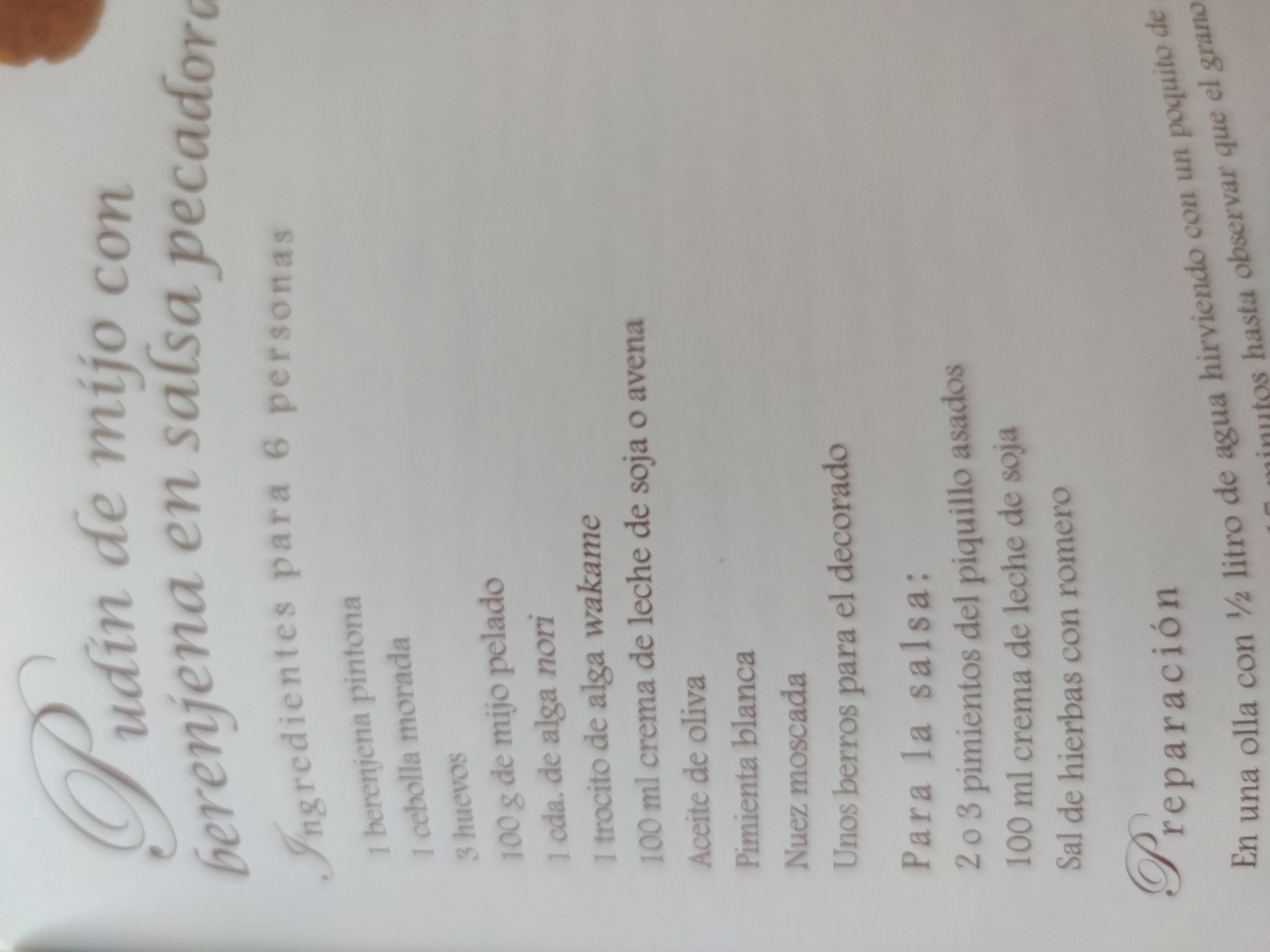 The image shows a page from a cookbook, featuring a recipe titled "Pudin de mijo con berenjena en salsa pecadora," which translates to "Millet pudding with eggplant in sinful sauce." The recipe lists ingredients for 6 people, including:
* 1 pintona eggplant
* 1 purple onion
* 3 eggs
* 100 g of peeled millet
* 1 tbsp. of nori seaweed
* 1 piece of wakame seaweed
* 100 ml cream of soy or oat milk
* Olive oil
* White pepper
* Nutmeg
* Some watercress for decoration
The recipe also includes a section for the sauce ingredients:
* 2 or 3 roasted piquillo peppers
* 100 ml cream of soy milk
* Herb salt with rosemary
The bottom of the page starts to detail the preparation instructions, indicating that it begins with boiling ½ liter of water in a pot with a bit. The background is white, and the text is in a beige color.