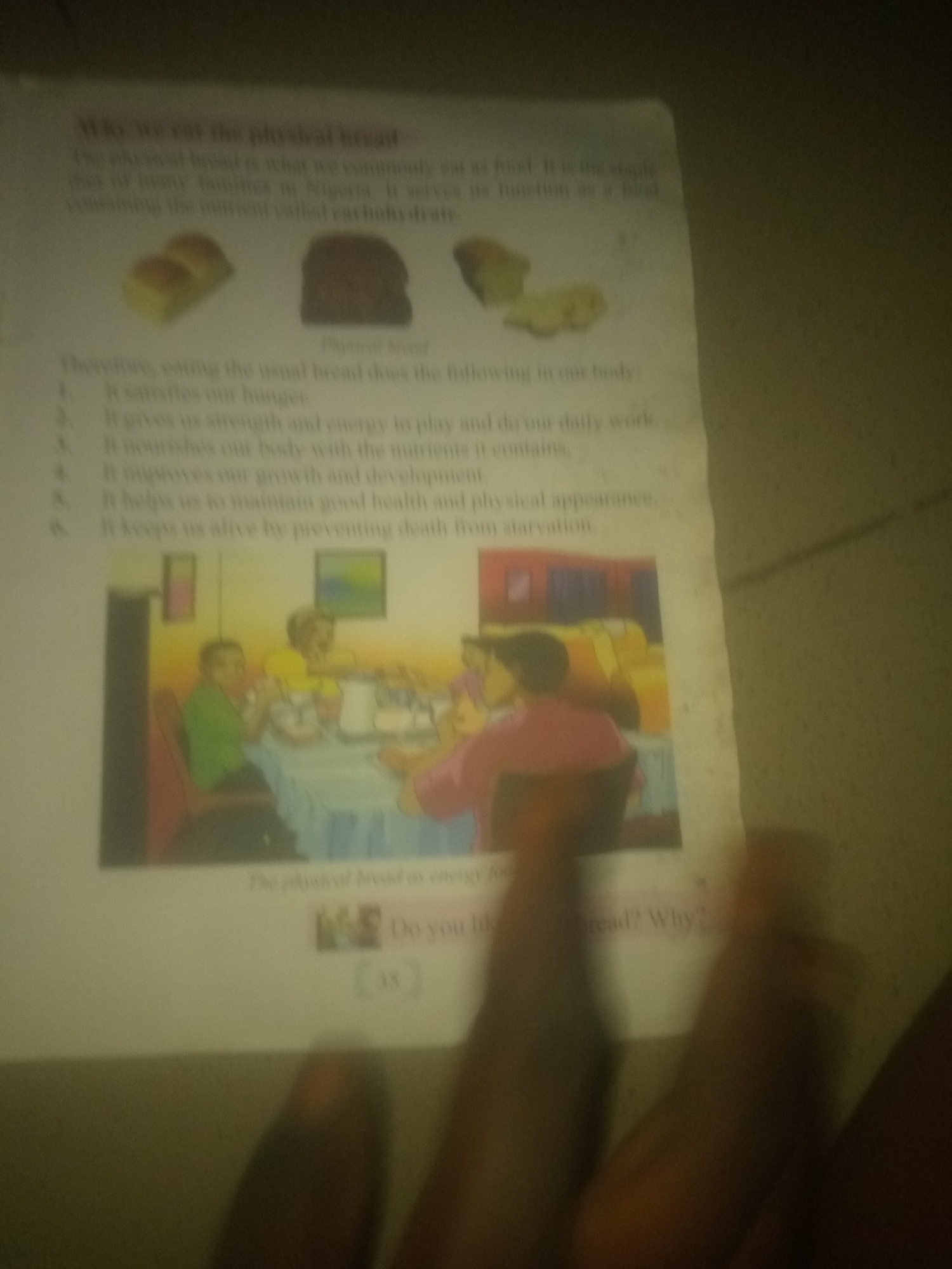 The image displays a page from a textbook, or similar educational material, featuring text and an illustration related to bread. The text discusses "why we eat the physical bread" and lists several reasons, such as satisfying hunger, providing strength and energy, nourishing the body, improving growth and development, and keeping us alive by preventing starvation. An illustration depicts a family or group of people sitting around a table, seemingly eating. To the top of the page, there are images of different types of bread. The overall scene is a close-up, slightly blurry view of the document, with some hands visible in the foreground. There is no information in the image or the provided context that indicates the location in the city of Jauro Yinu, Nigeria.