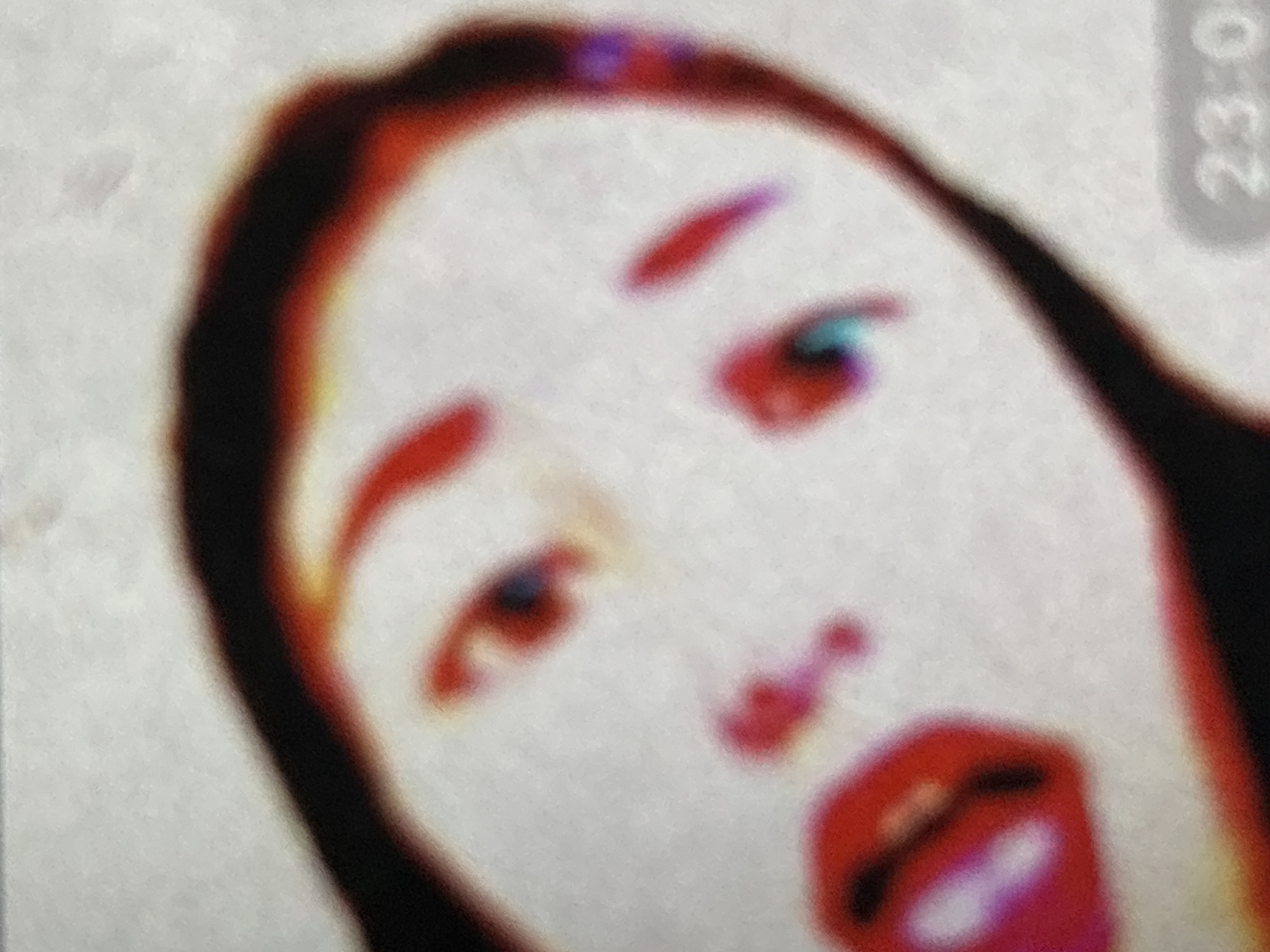 The image is a close-up, abstract, and digitally altered photograph of a human face. The face is tilted, with distorted features and vibrant, saturated colors, predominantly reds, blacks, and whites, with hints of blue and purple. The eyes are discernible as dark shapes with lighter centers, and the lips are a bright, glossy red. The overall effect is impressionistic, with soft edges and a painterly quality. The background is a textured white. In the lower right corner, a digital timestamp reads "23:0". The image does not contain any identifiable landmarks or elements that would suggest its location in Orihuela, Spain.