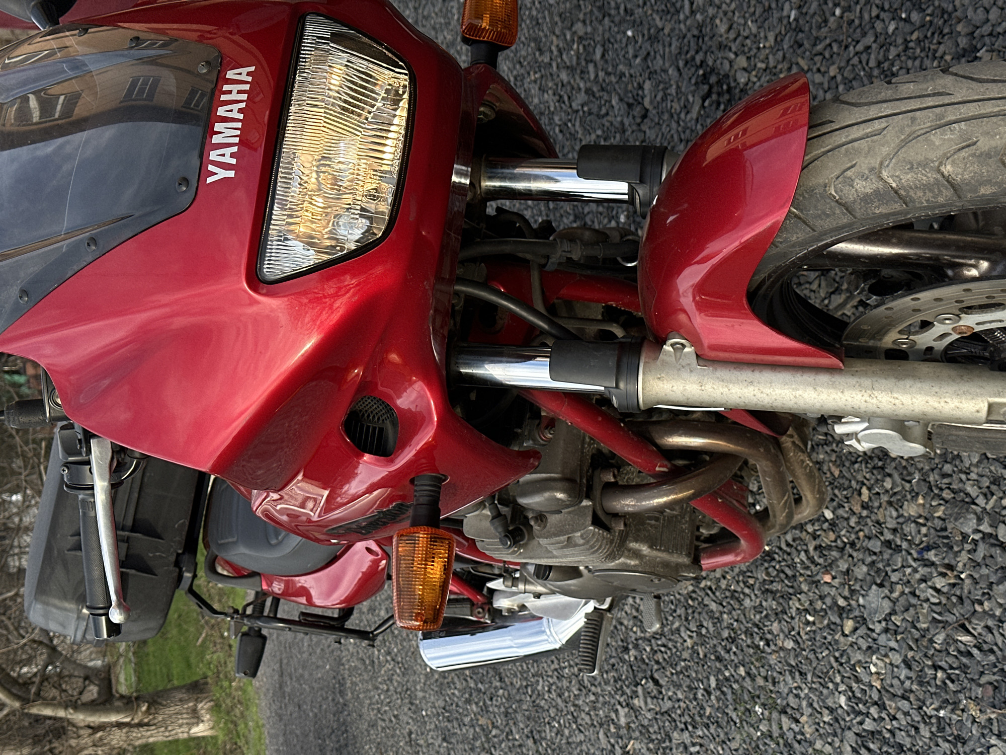 The image shows the front of a red Yamaha motorcycle parked on a surface of small gray gravel. The motorcycle's headlight and front fender are visible, as are the front tire and suspension. The location is unknown and there are no indications it is Rostov-on-Don, Russia. No people or actions are visible in the image.