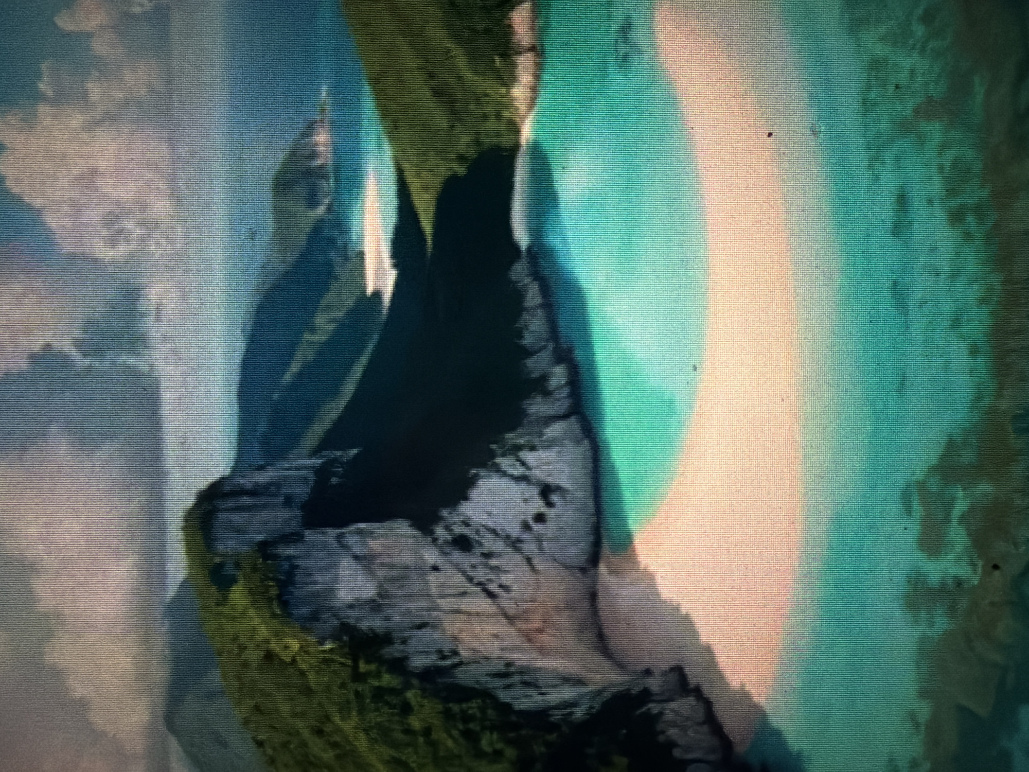 This media file depicts a scenic view of what appears to be a coastal landscape. The primary subjects are dramatic rock formations and the surrounding water and sky. The rock formations are jagged and appear to be covered in patches of green vegetation, suggesting a rugged, natural environment.
The scene is bathed in an ethereal light, with a prominent, soft-edged oval of bright, almost pastel, turquoise and peach hues dominating the right side of the image. This unusual lighting creates a dreamlike atmosphere. There are also areas of soft, diffused light that could be interpreted as clouds or mist, particularly on the left side of the image, tinged with blues and whites.
The overall impression is one of natural beauty and perhaps a touch of mystery due to the diffused and colorful lighting. There are no people or man-made objects clearly visible. The activity or event taking place is not evident; it is a still, observational shot of the landscape.
Notable details include the strong contrast between the dark, textured rock and the luminous, soft-colored areas. The texture of the image suggests it might be a photograph displayed on a screen, possibly with some digital artifacting or intentional artistic filtering. The time of day is difficult to ascertain precisely due to the unusual lighting, but the soft light could suggest either sunrise, sunset, or a heavily overcast day with atmospheric effects. The location context provided, Baan Mae Nam, Thailand, points towards a tropical or subtropical coastal setting, which aligns with the visual elements of greenery on rocks and water. No text is visible in the image.