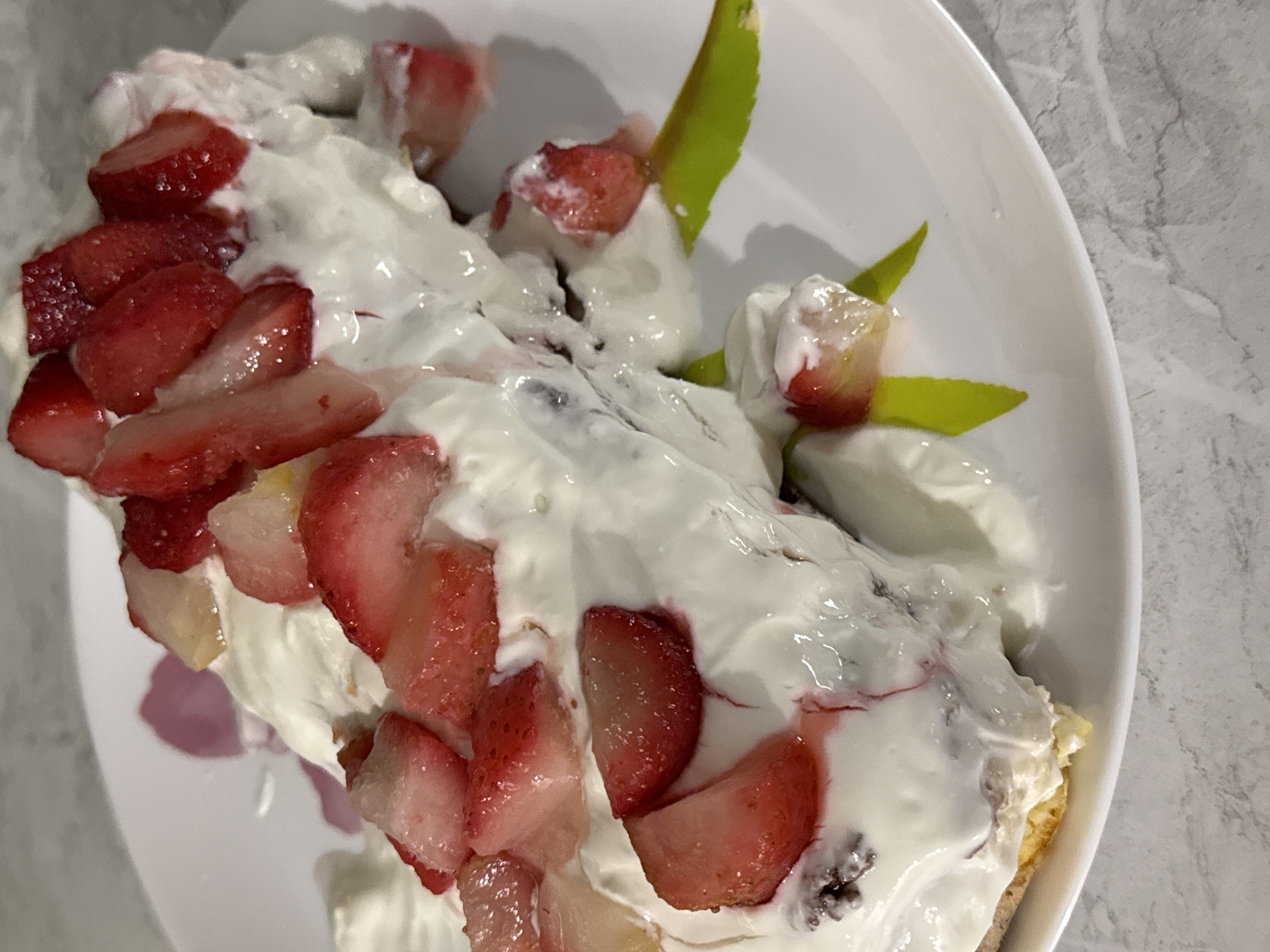 A dessert featuring whipped cream and sliced strawberries is displayed on a white plate. The plate rests on a surface with a marbled or stone-like pattern. There is no contextual evidence to confirm that the image was taken in Chaikovsky, Russia.