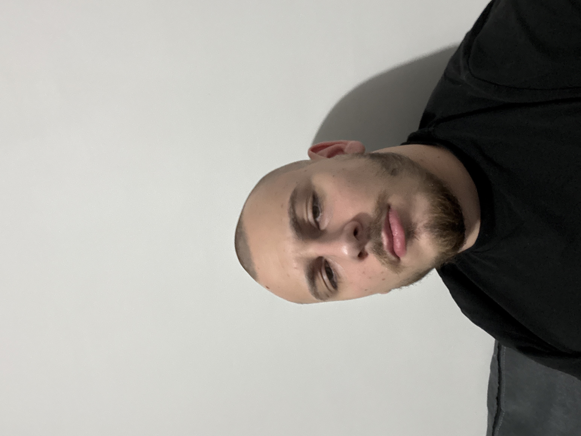 A close-up, angled view of a bald man with a short beard and mustache, wearing a black t-shirt. He is positioned against a plain white wall. There is no indication of the city of Stara Zagora, Bulgaria, in the image.