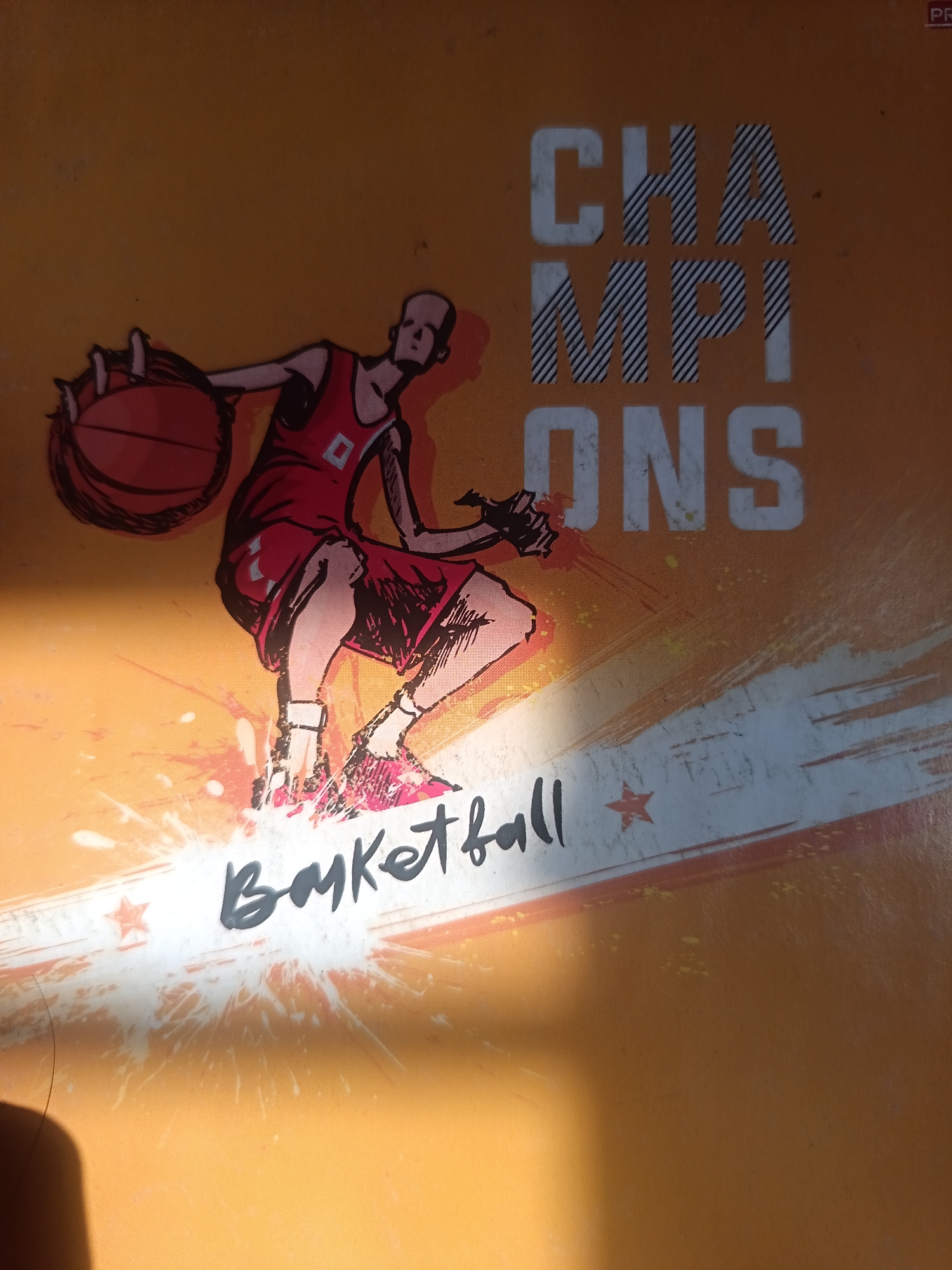 The image shows a graphic design for "CHAMPIONS BASKETBALL" on an orange background. A stylized illustration of a basketball player in mid-action, dribbling a ball, is prominent. The text "CHAMPIONS" is displayed in large, bold, white lettering with a diagonal striped pattern within the letters. Below, "BASKETBALL" is written in a handwritten script style. The background features abstract splashes and lines in white, orange, and pink, suggesting dynamism. The overall aesthetic is energetic and sporty. There is no information in the image that can be used to determine its location in Novokuznetsk, Russia.