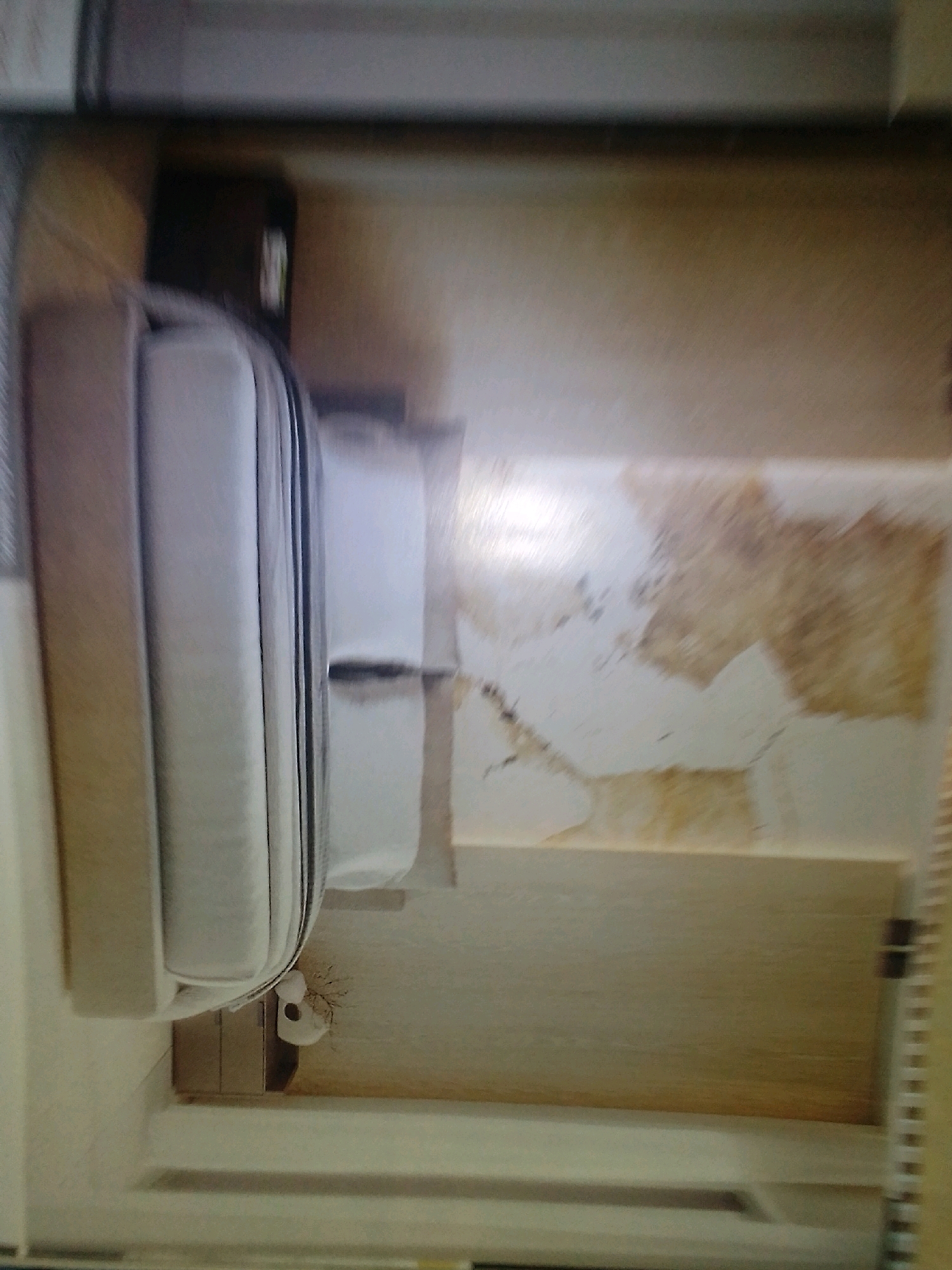 The image depicts the interior of a drawer. The drawer contains a white mattress or cushion, folded over. To the left of the mattress is a brown object, possibly a box. To the right of the mattress, the drawer's interior surface shows water stains and discoloration. The overall environment suggests a residential or storage space. The image quality is poor and blurry, making precise identification of all elements difficult. No specific location in Winterveld, South Africa, can be determined from the visual information provided.