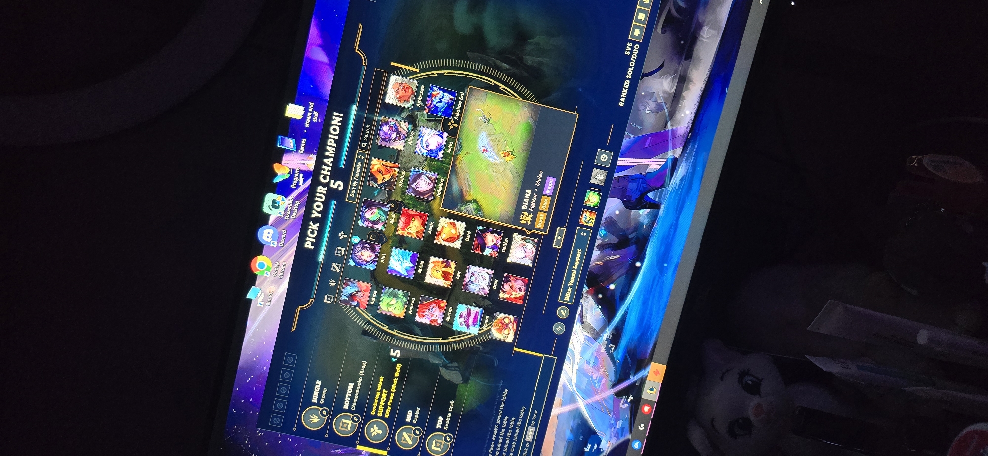 The image shows a computer screen displaying the champion selection screen for the game League of Legends. The player is in a ranked solo/duo queue and currently has 5 seconds to pick a champion. The available champions are displayed in a circular interface. The player has selected "Diana" as their champion, who is classified as a fighter/melee champion. Below the champion selection screen, the declared intents of other players are listed, with "Kitty Paws" declaring for Support. The operating system desktop is visible in the background, showing icons for programs such as Google Chrome, Discord, Streamlabs Desktop, and several games. The physical environment around the screen includes a white ring light and desk clutter including a small white stuffed toy. There is no evidence to indicate the image was taken in Burgas, Bulgaria.