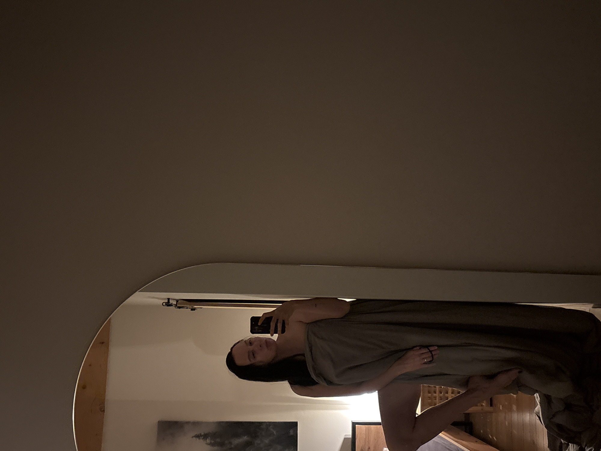 A mirror selfie depicts a woman wrapped in a sheet, holding a smartphone. The background reveals a room interior, including wall decor and wooden furniture. The location is not discernible as Chaikovsky, Russia.