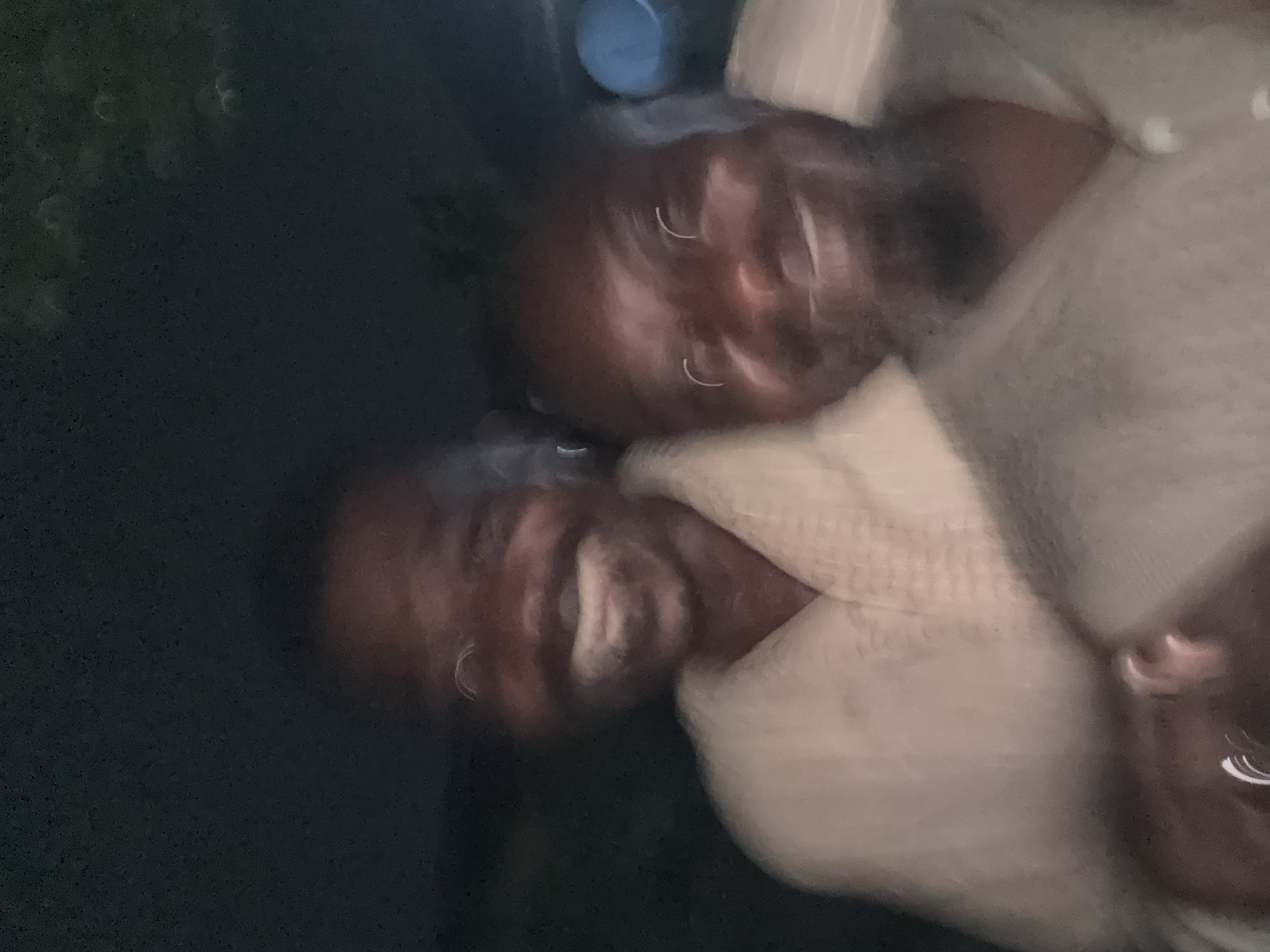 The image appears to show three blurred faces, possibly of adults, with dark skin. They are wearing light-colored clothing that may be made of a woven fabric. The background is dark, possibly indicating an outdoor location at night or in a dimly lit area. It's difficult to ascertain more precise details due to the blurry nature of the image. It is impossible to verify if this photo was taken in Ado, Nigeria, without more information.