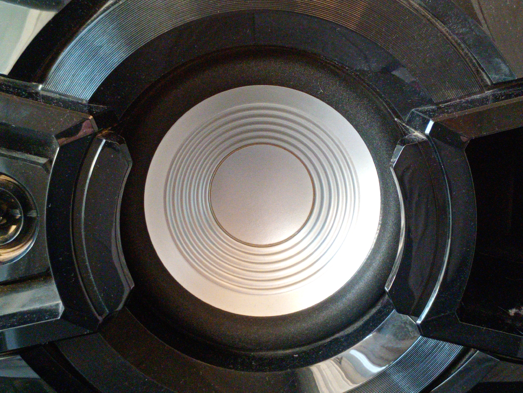 The image shows a close-up view of a speaker. The speaker cone is silver with concentric rings. The surround is black. The speaker is mounted in a black housing with a glossy finish. The location in the city of Roza, Bulgaria is unknown.