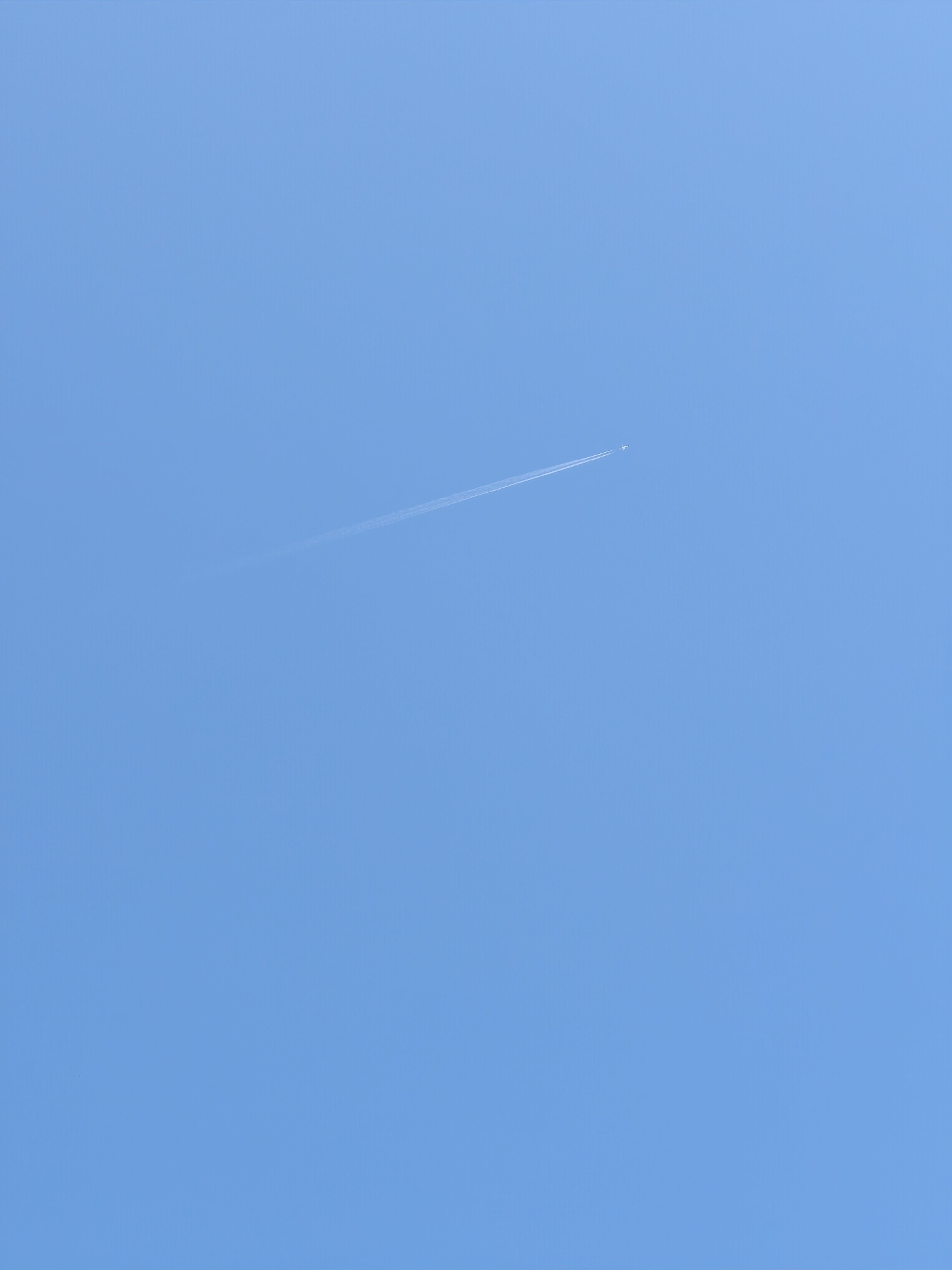 The image shows a clear blue sky with a faint contrail from an airplane. The contrail is a thin white line stretching diagonally across the upper right portion of the frame. There is no discernible urban environment, buildings, or people visible in the image. The location in Castiglione della Pescaia, Italy, is not identifiable from the visual content of the photograph.