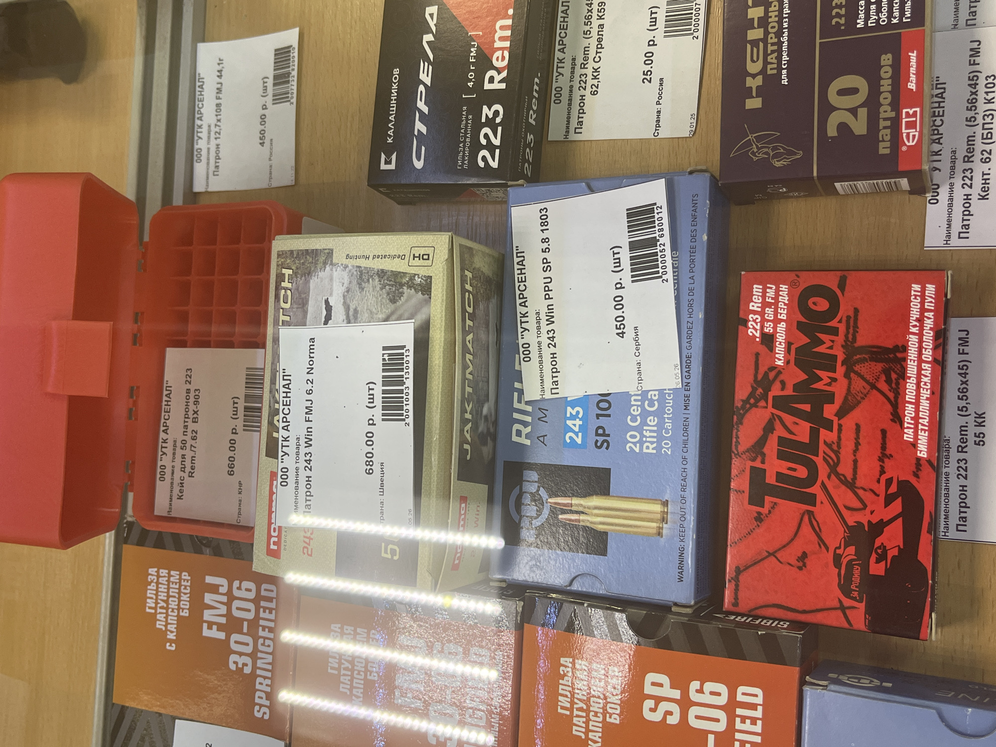 The image displays a retail display of ammunition boxes in a store, likely a gun or sporting goods shop. The products are varied, with different calibers and brands visible, including "FMJ 30-06 SPRINGFIELD," ".223 Rem," and "TULAMMO." Some of the packaging includes Russian text, indicating it is a store in Russia. The specific location in Yekaterinburg, Russia, cannot be determined from the image alone. There are no people visible in the image. The lighting suggests an indoor retail environment.