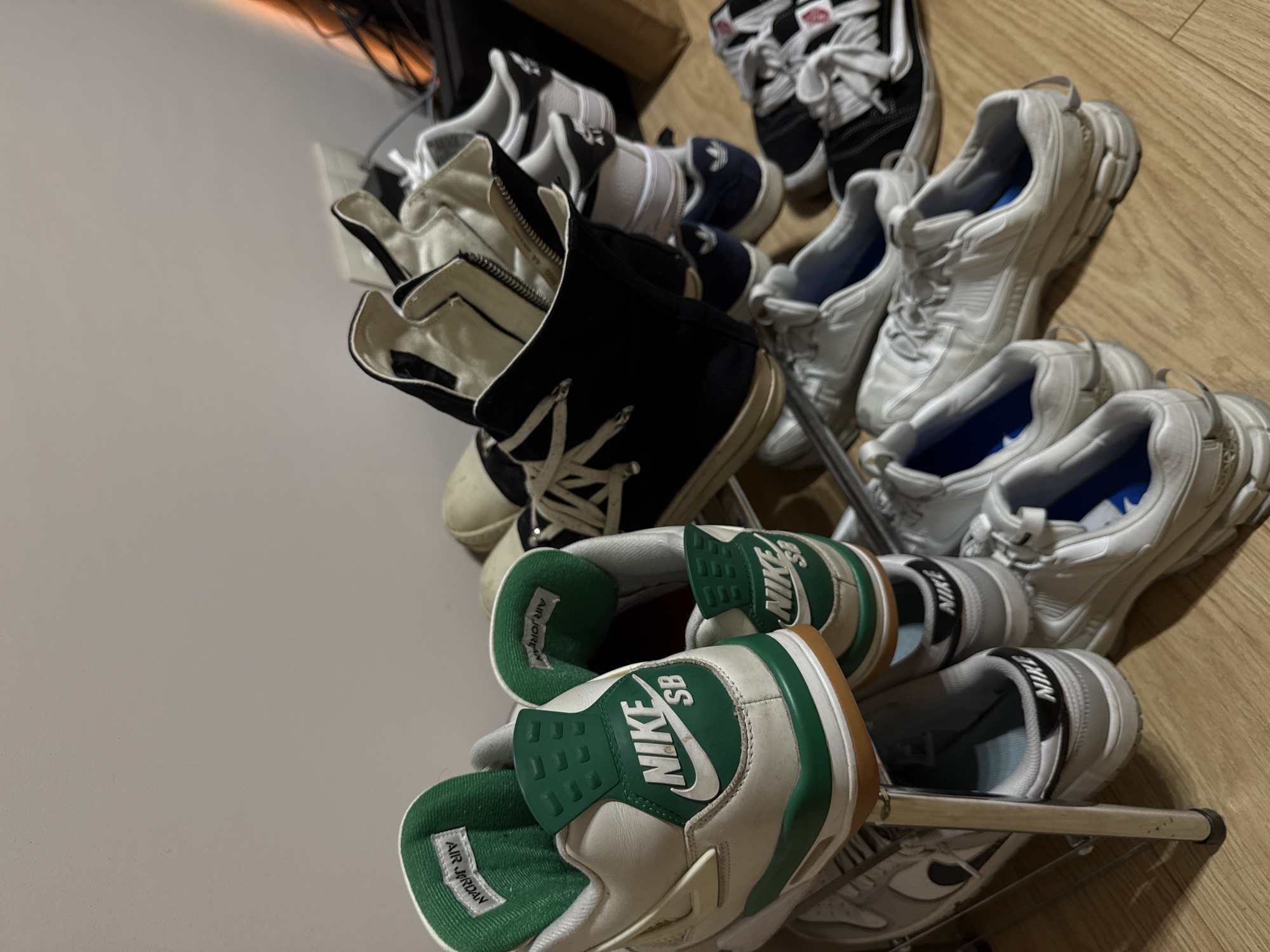 The image shows a variety of shoes on a metal shoe rack. There are pairs of Air Jordan sneakers with green accents, a pair of black Rick Owens high-tops with cream soles, and a few pairs of white sneakers. The location cannot be determined to be Sofia, Bulgaria from the image.