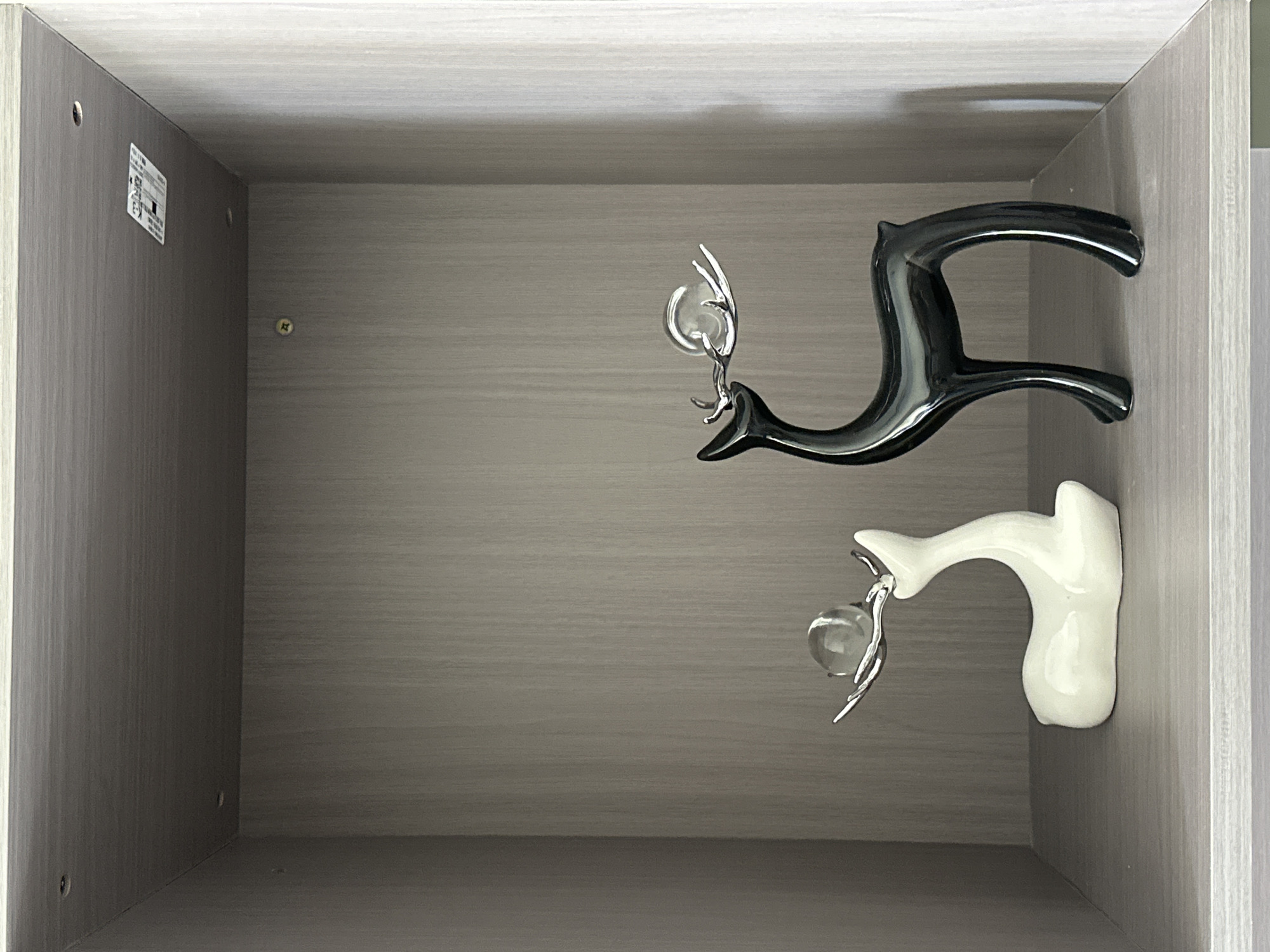 A top-down shot of an open, empty gray wooden drawer. Two decorative objects, shaped like stylized birds or dolphins holding a clear ball, are resting against the right side of the drawer. One is black and the other is white. The scene shows no people or activities. There is a label on the left interior wall of the drawer.
I cannot determine the location in Chongqing High-tech Zone, China from this image.