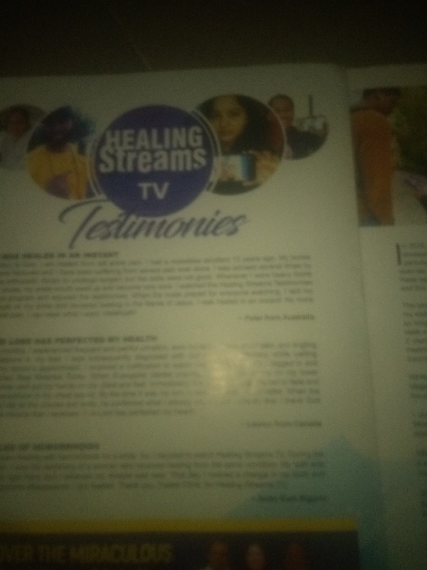 The image is a blurry photograph of a magazine page, featuring the "Healing Streams TV" logo and several testimonials. One testimonial is from Jauro Yinu, Nigeria, detailing a personal healing experience. The content appears to be religiously themed, focusing on miraculous healing. The overall quality of the image is poor, with significant blur and low resolution, making it difficult to discern fine details of the people or the environment in the photographs within the magazine. There are no identifiable elements that place the image within a specific city or city district.