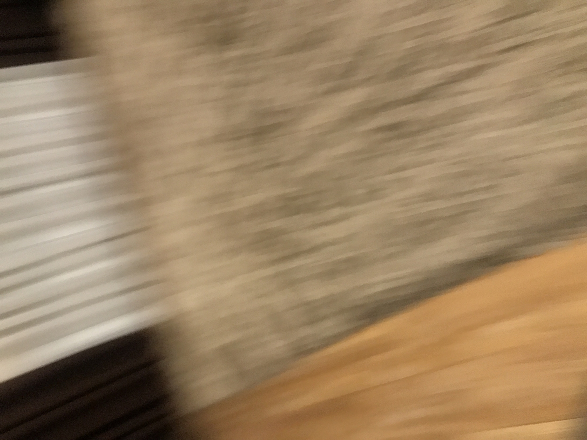 The image is blurry and lacks detail, making precise identification difficult. However, based on the available visual information, here's what can be inferred:
* **Objects:** The image contains indistinct forms suggestive of multiple objects. There is a white linear pattern on the left, possibly a white blind or shutter. A tan background occupies the upper right. A brown wooden plane occupies the bottom right.
* **Environment:** The overall impression suggests an indoor setting. The presence of blinds/shutters implies a window.
* **Location:** It is impossible to deduce the exact location in Yerevan, Armenia, due to the extreme blurriness.