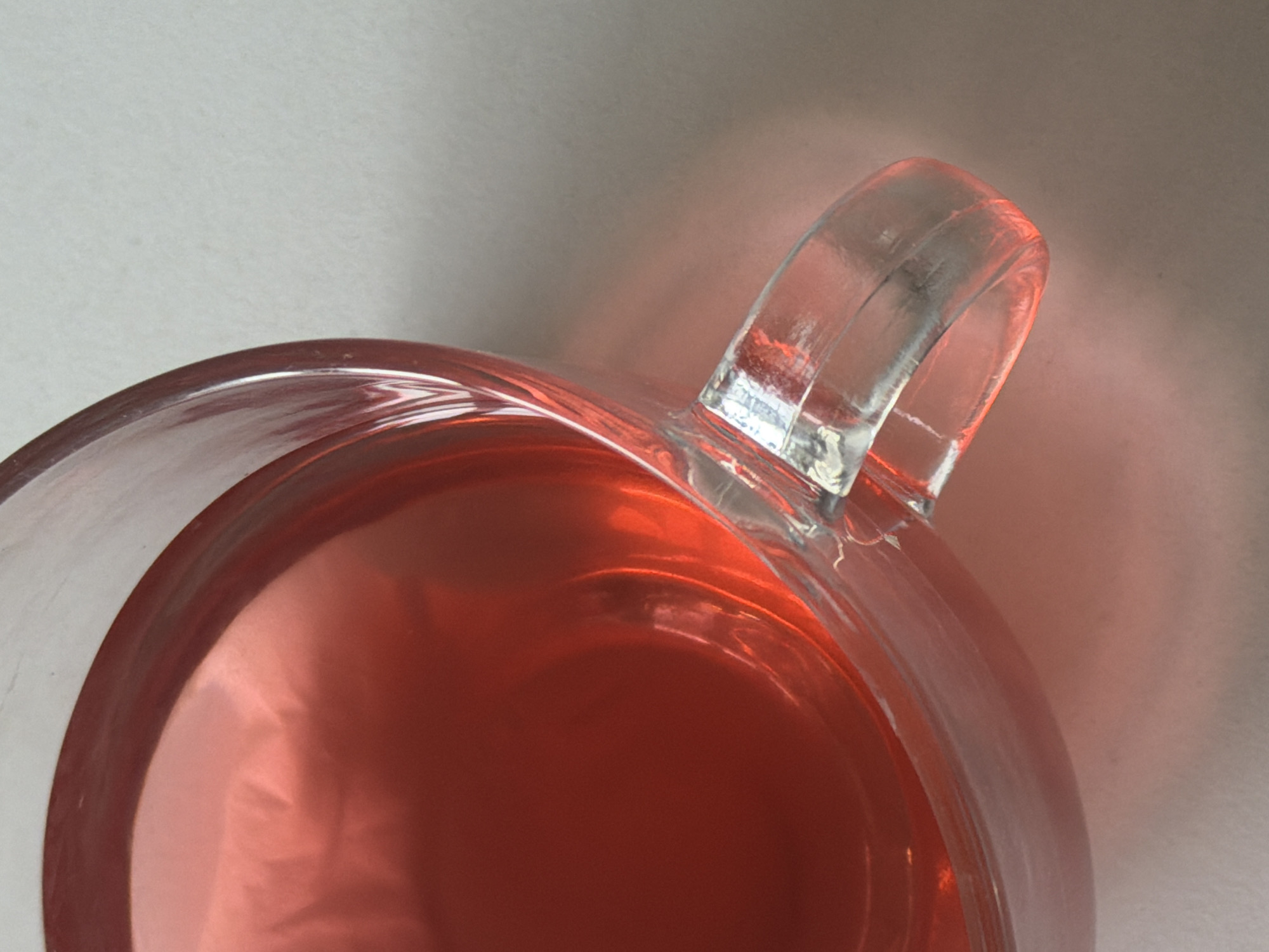 A close-up shot features a glass mug, partially filled with a reddish liquid. The mug has a clear handle, and the lighting creates a slight glare. The background is a light, neutral color. There is no indication of the location being Yerevan, Armenia.