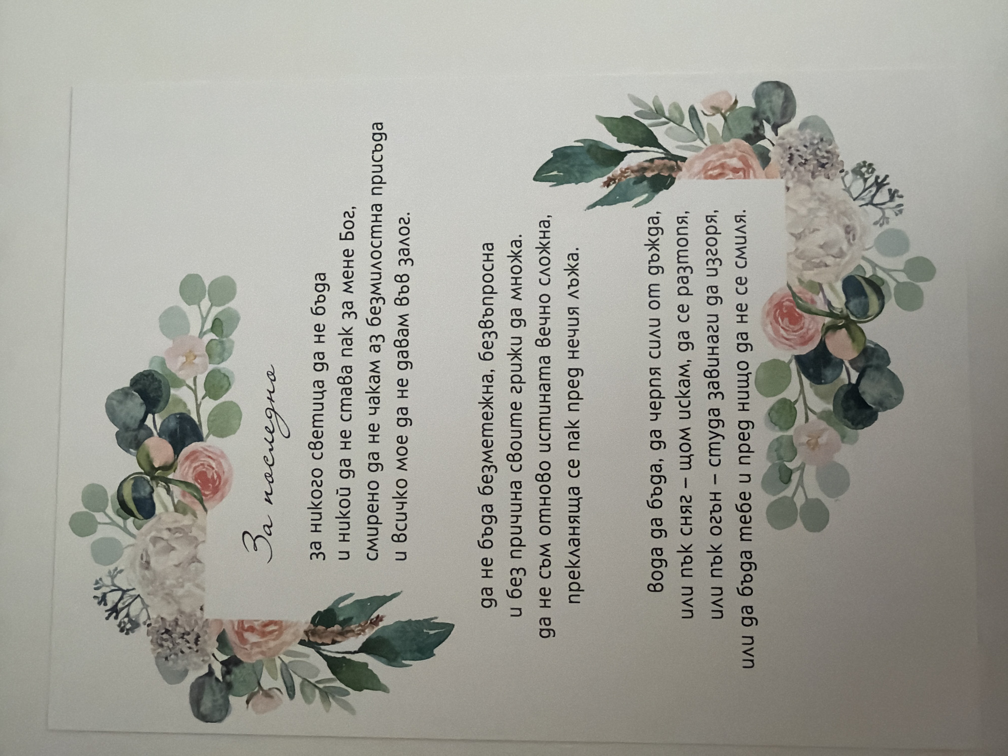 The image shows a white card with a floral border. The text on the card is in Bulgarian and appears to be a poem or a prayer. The floral design features a variety of flowers and greenery, including roses, eucalyptus leaves, and other delicate blooms. The text is centered on the card and is written in a script font. The overall impression is one of elegance and sentimentality. There is no information in the image that indicates its location in Pazardzhik, Bulgaria.